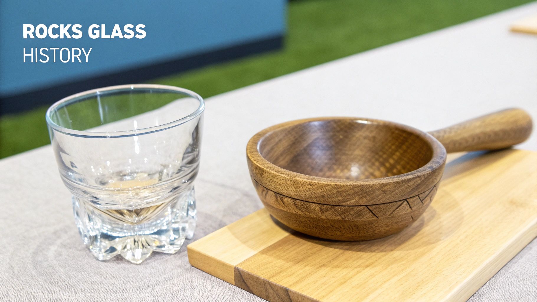 A clear rocks glass with a textured base, containing amber liquid, sits beside a wooden bowl and board.