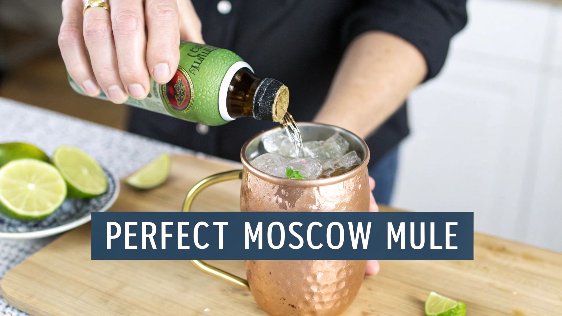 A person pouring a drink from a green bottle into a hammered copper Moscow mule mug with ice and lime, with fresh limes nearby.