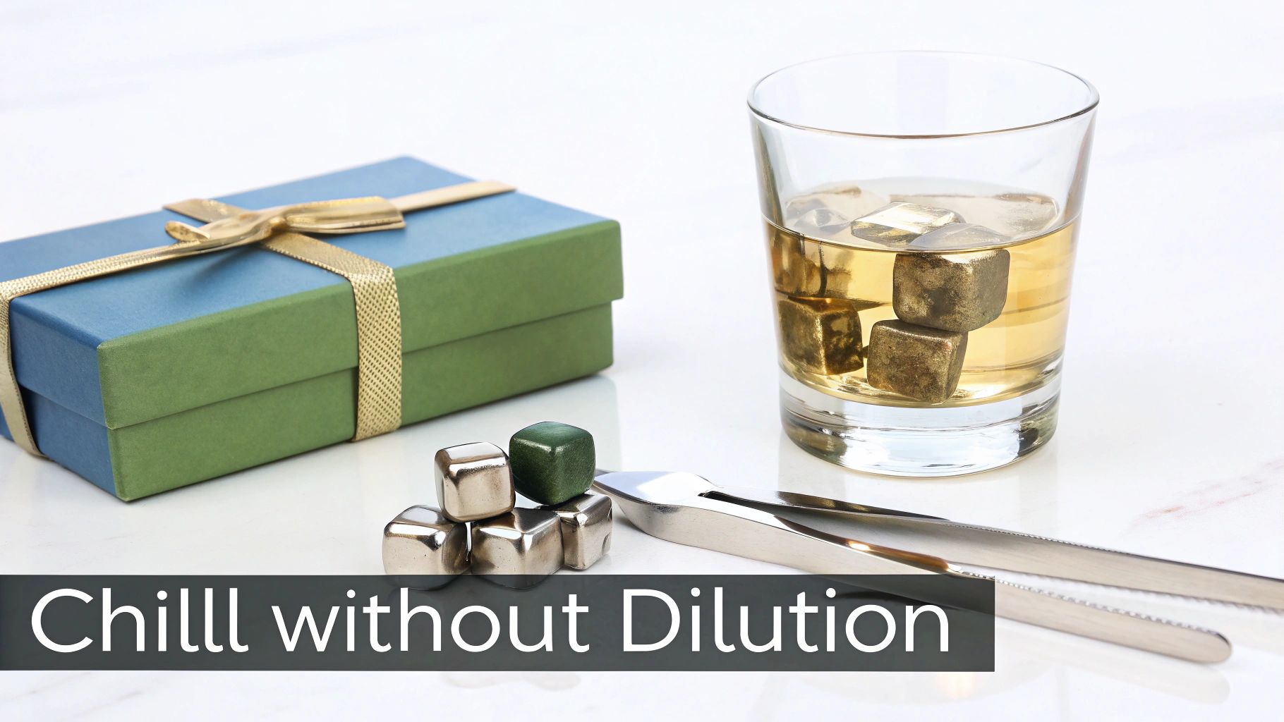 A gift box, whiskey glass with metal chilling cubes, tongs, and stone cubes on a white table.