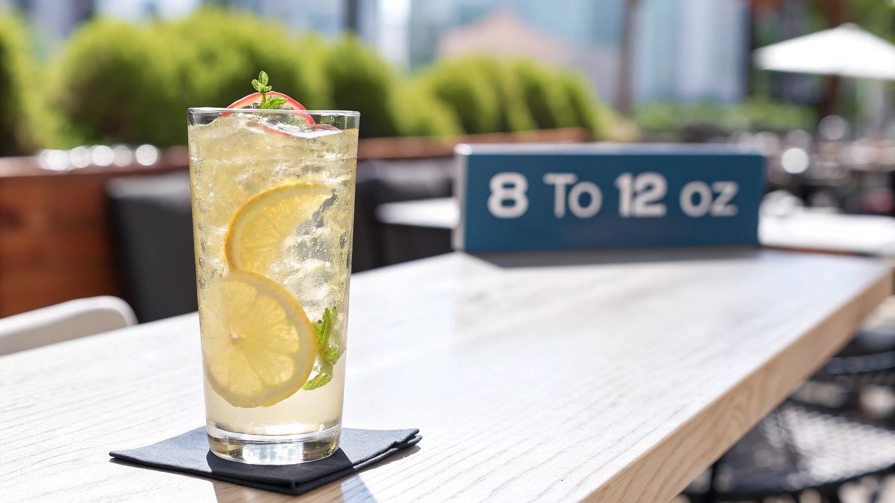 A refreshing highball glass of iced lemon drink with mint on a wooden outdoor table.