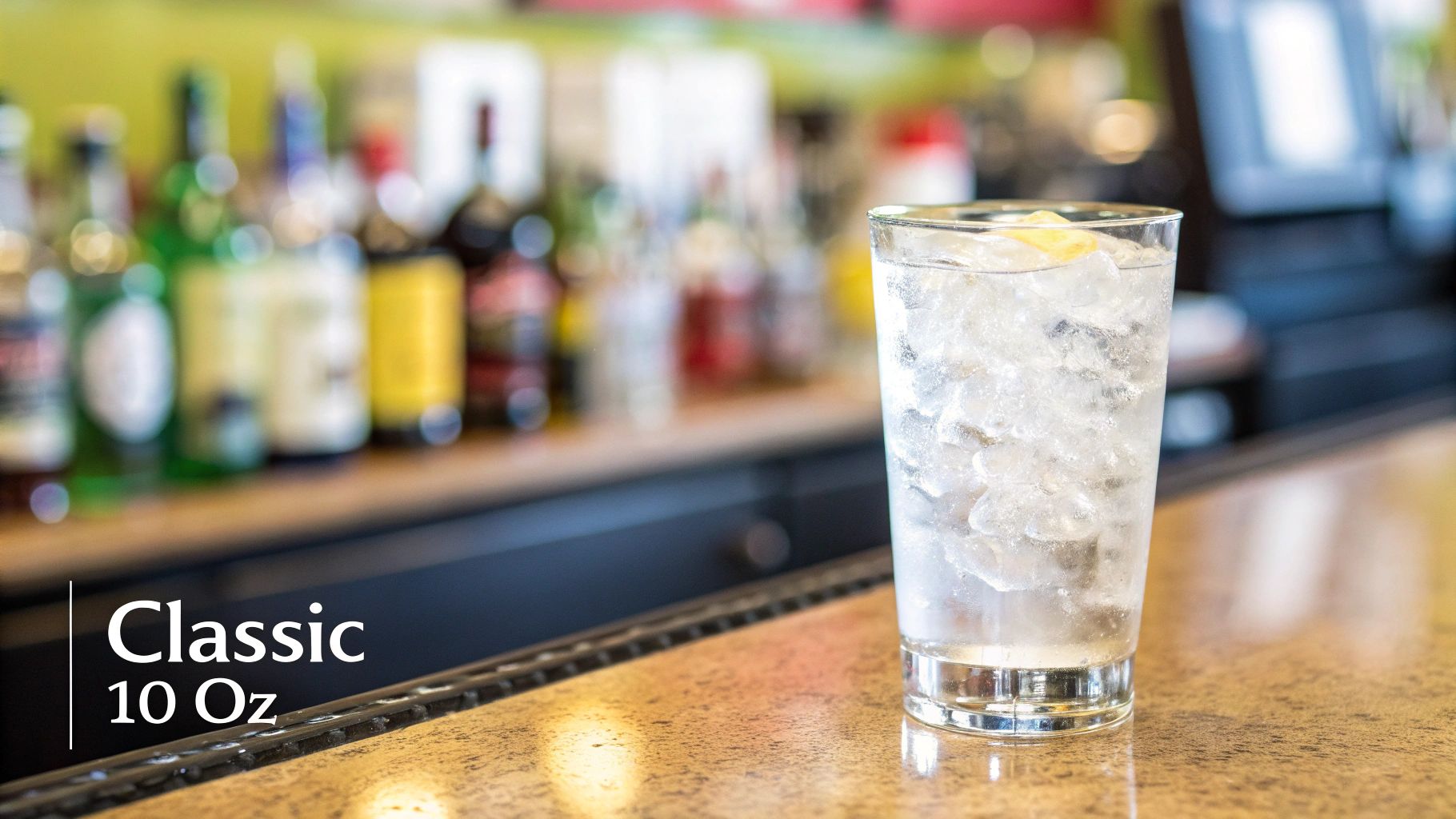 A clear highball glass filled with ice water and a lemon wedge on a blurred bar counter.