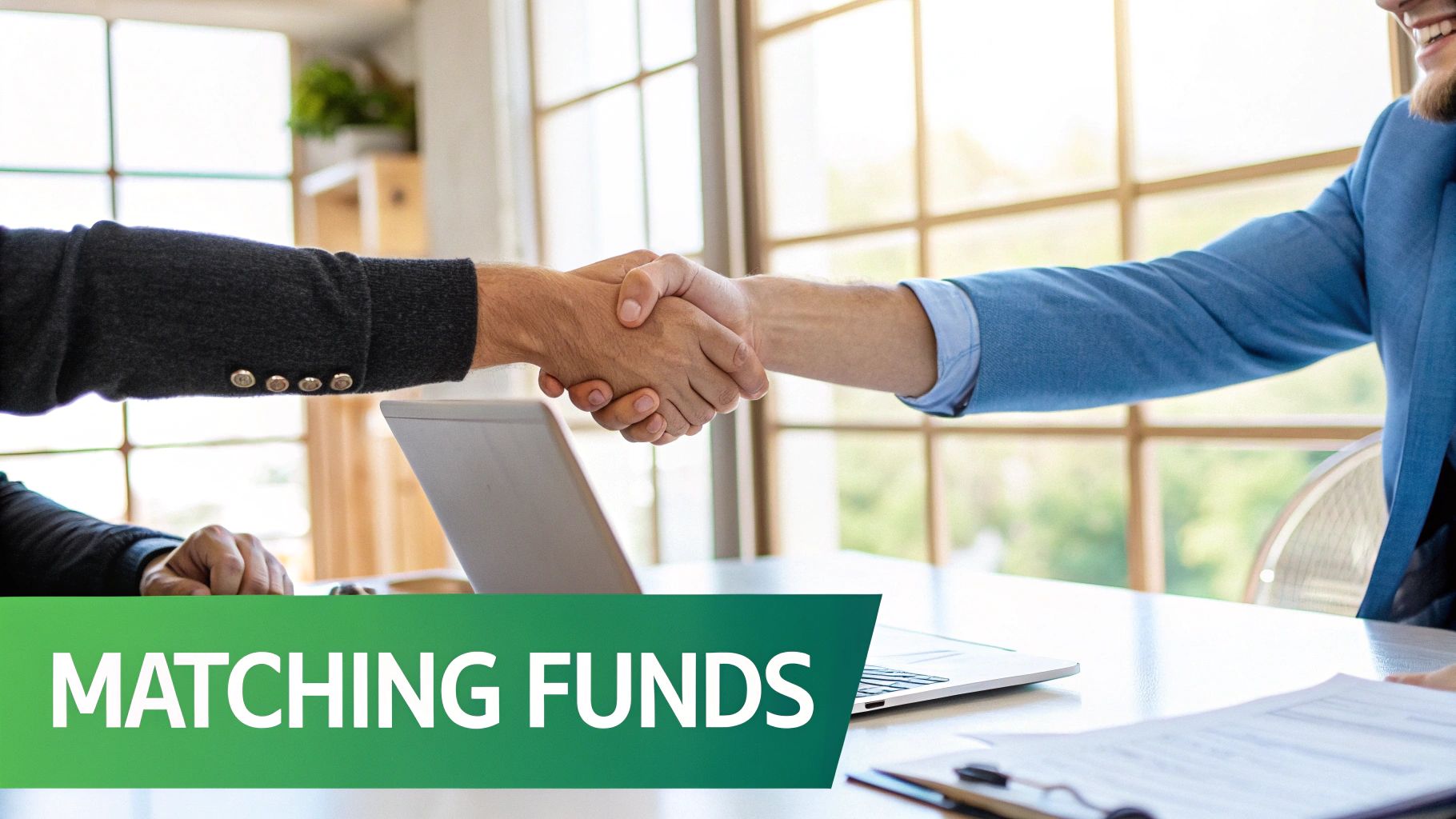 Two business people shaking hands over a table with a laptop, signifying a matching funds agreement.