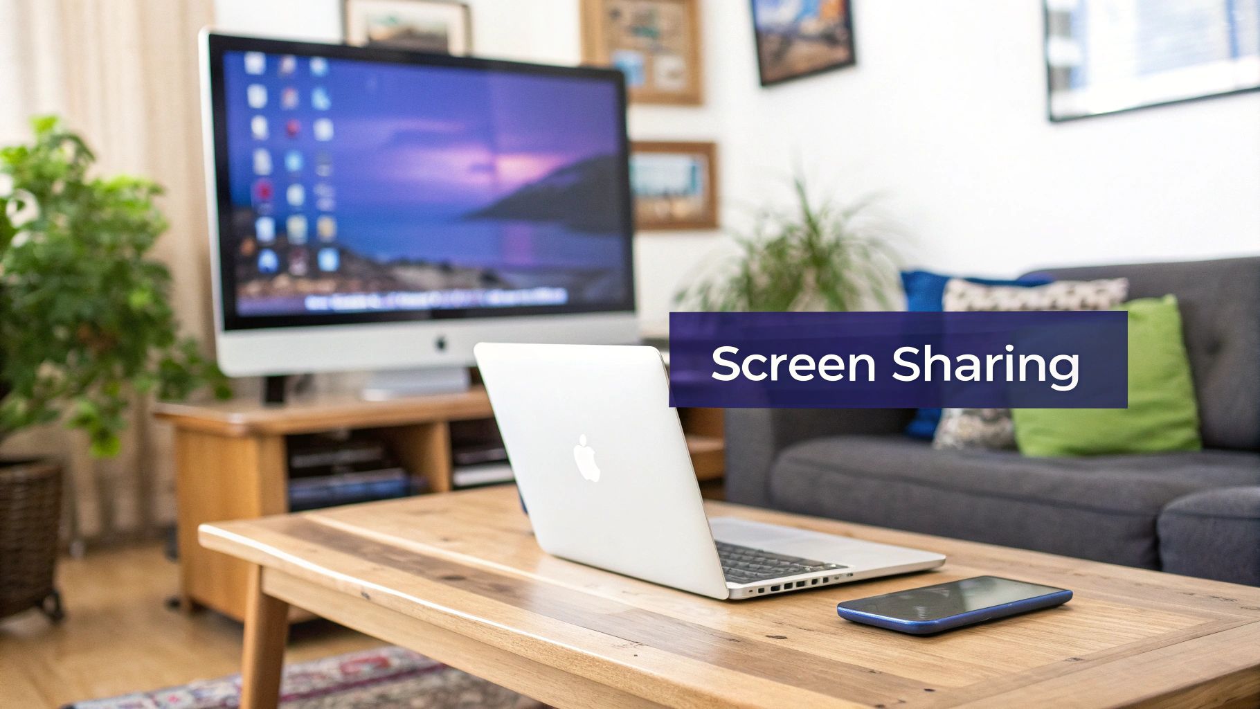A MacBook laptop and smartphone on a coffee table in a living room with an iMac desktop.
