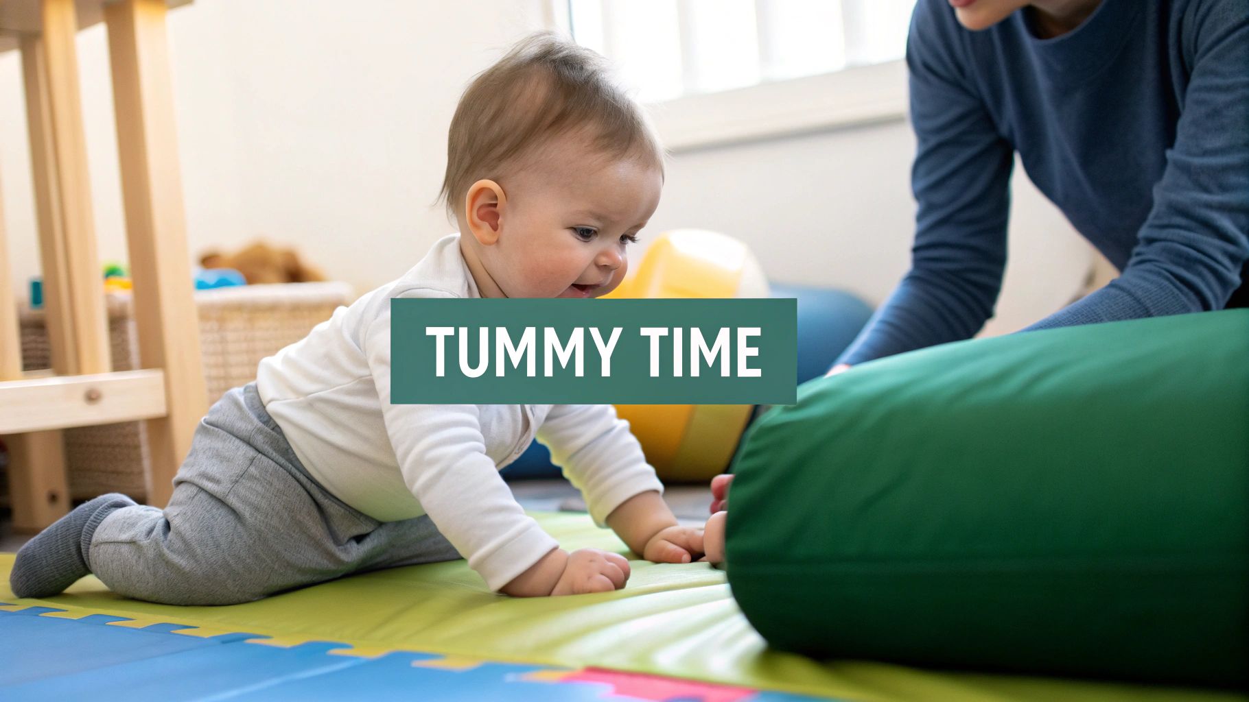 A happy baby is engaged in tummy time on a colorful play mat with an adult.