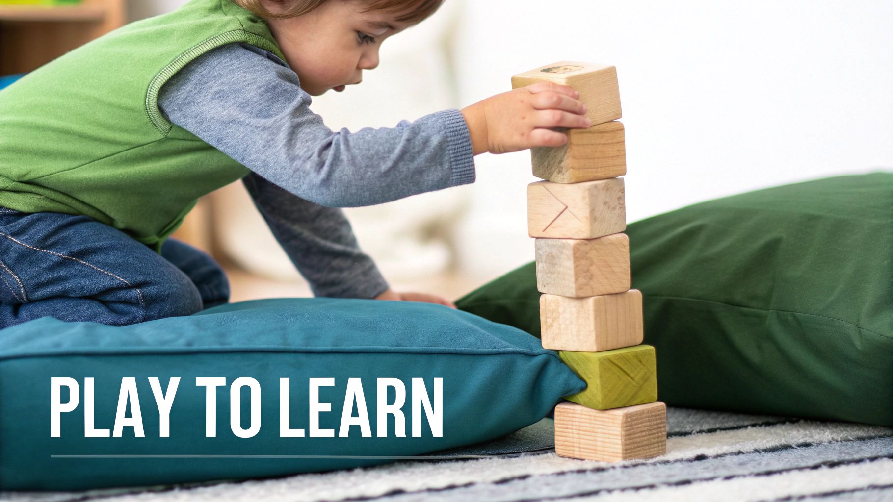 A young child concentrates while building a tall tower with wooden blocks on a cushion, with 'PLAY TO LEARN' text.