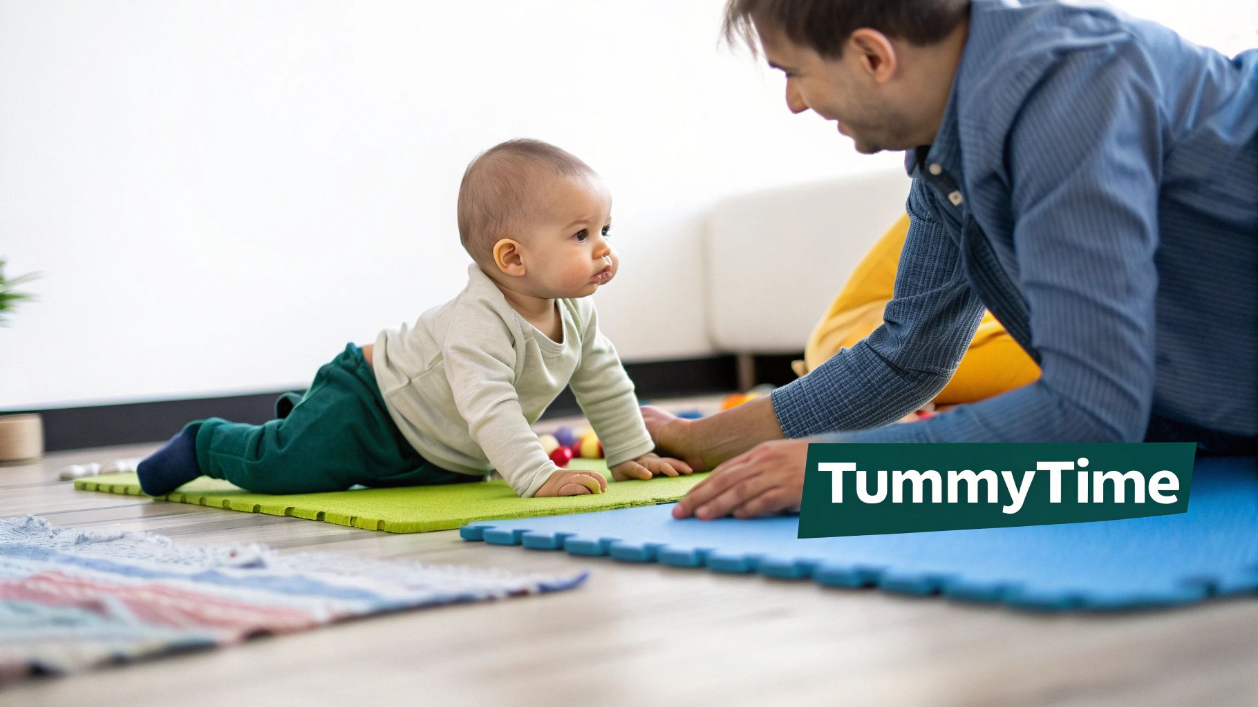 A baby on a green playmat looking up at an adult during tummy time.
