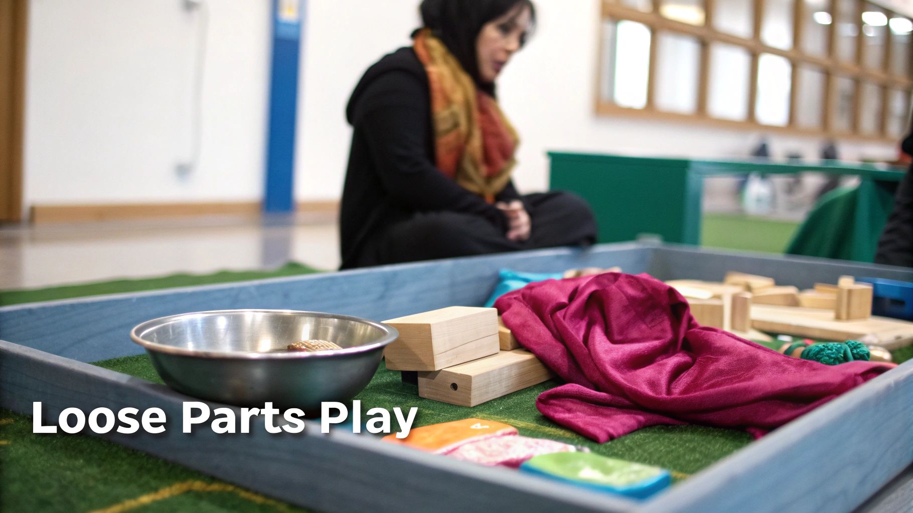 A child sits on the floor, deeply focused on exploring various heuristic play items from a basket.