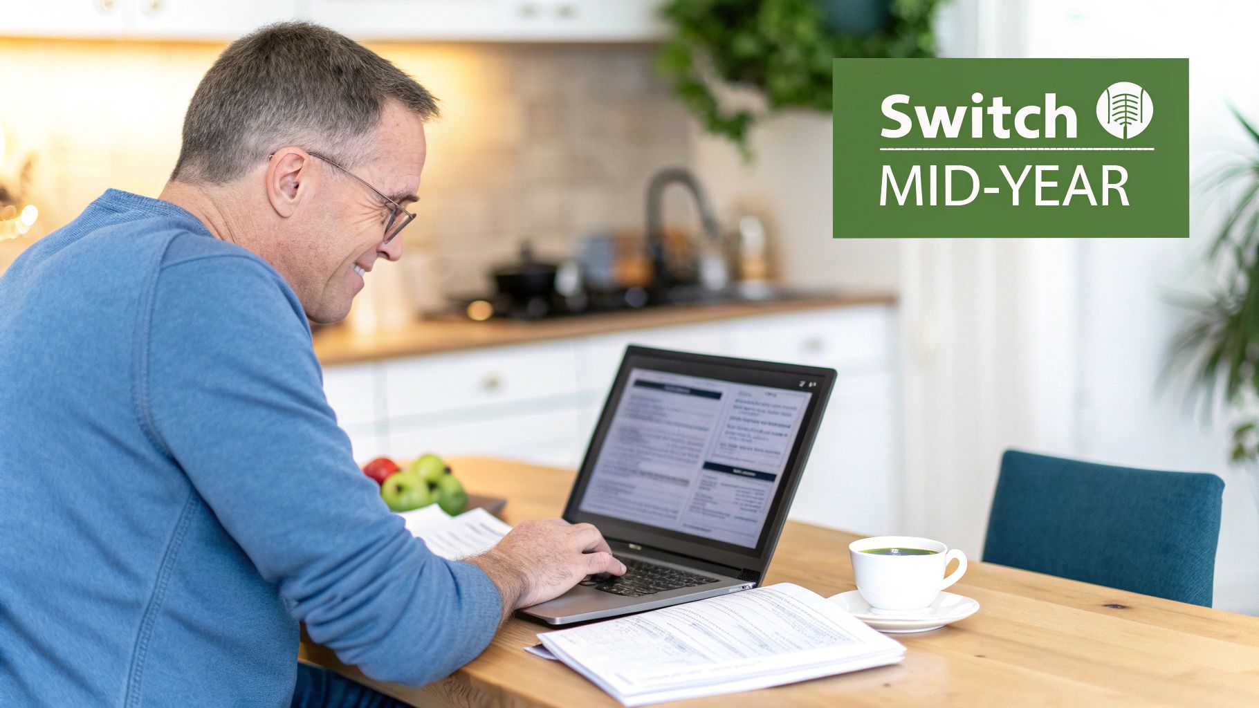 A smiling man in a blue shirt works on a laptop at a wooden table, with a 'Switch MID-YEAR' banner.