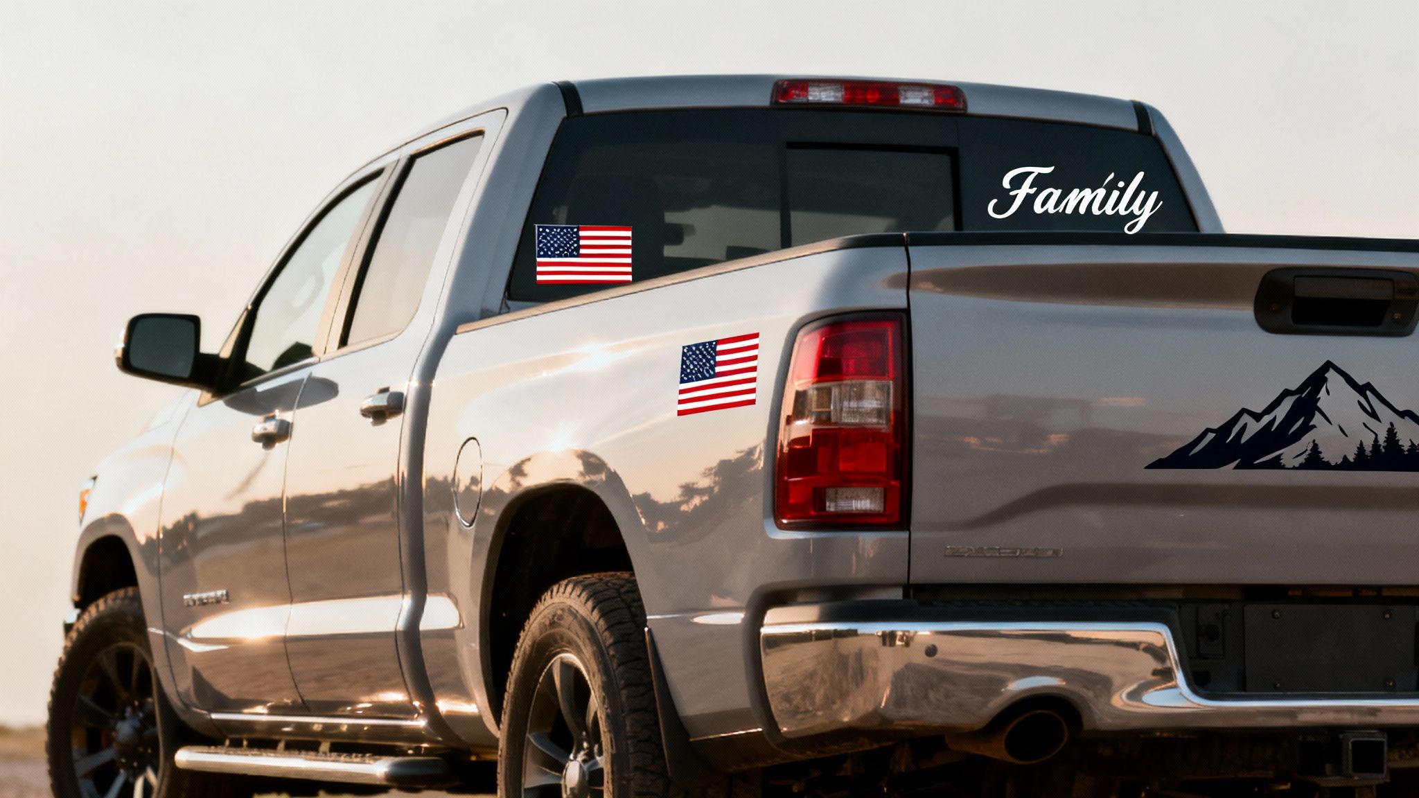 A silver pickup truck with a 'Family' decal, American flag stickers, and a mountain range graphic.