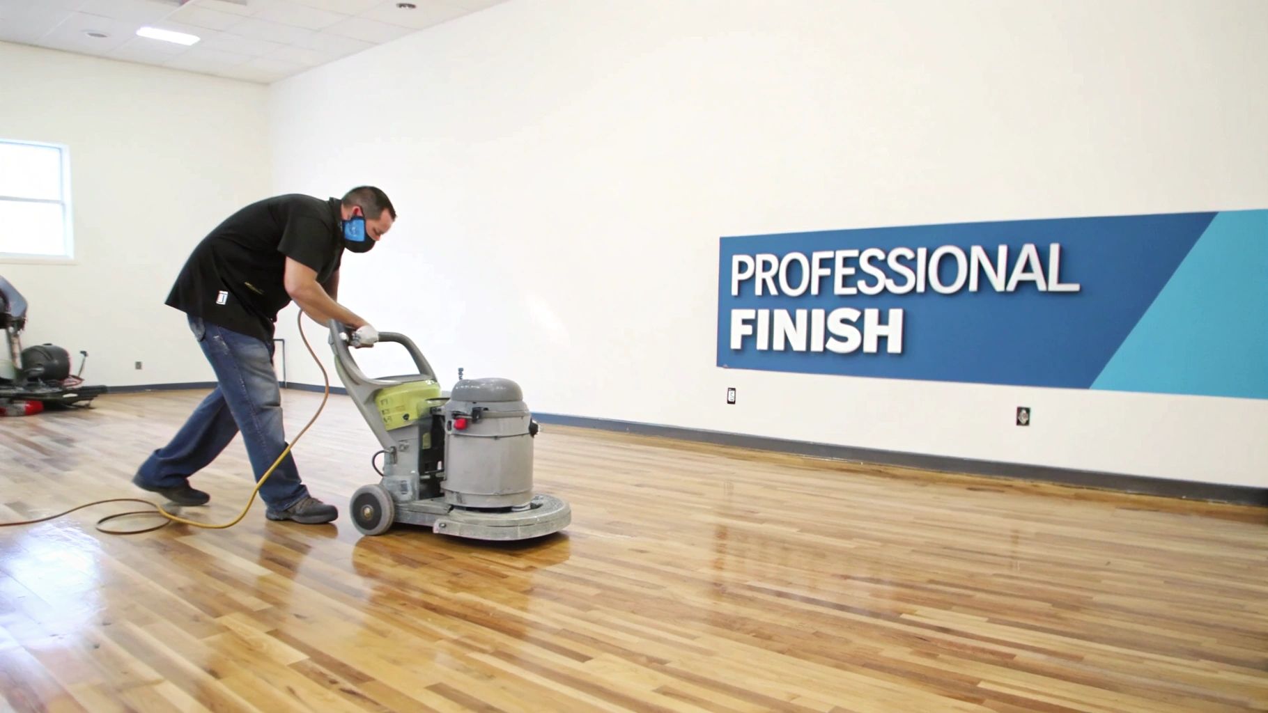 A man in a black shirt and jeans operates a floor buffer on a shiny hardwood floor, ensuring a professional finish.