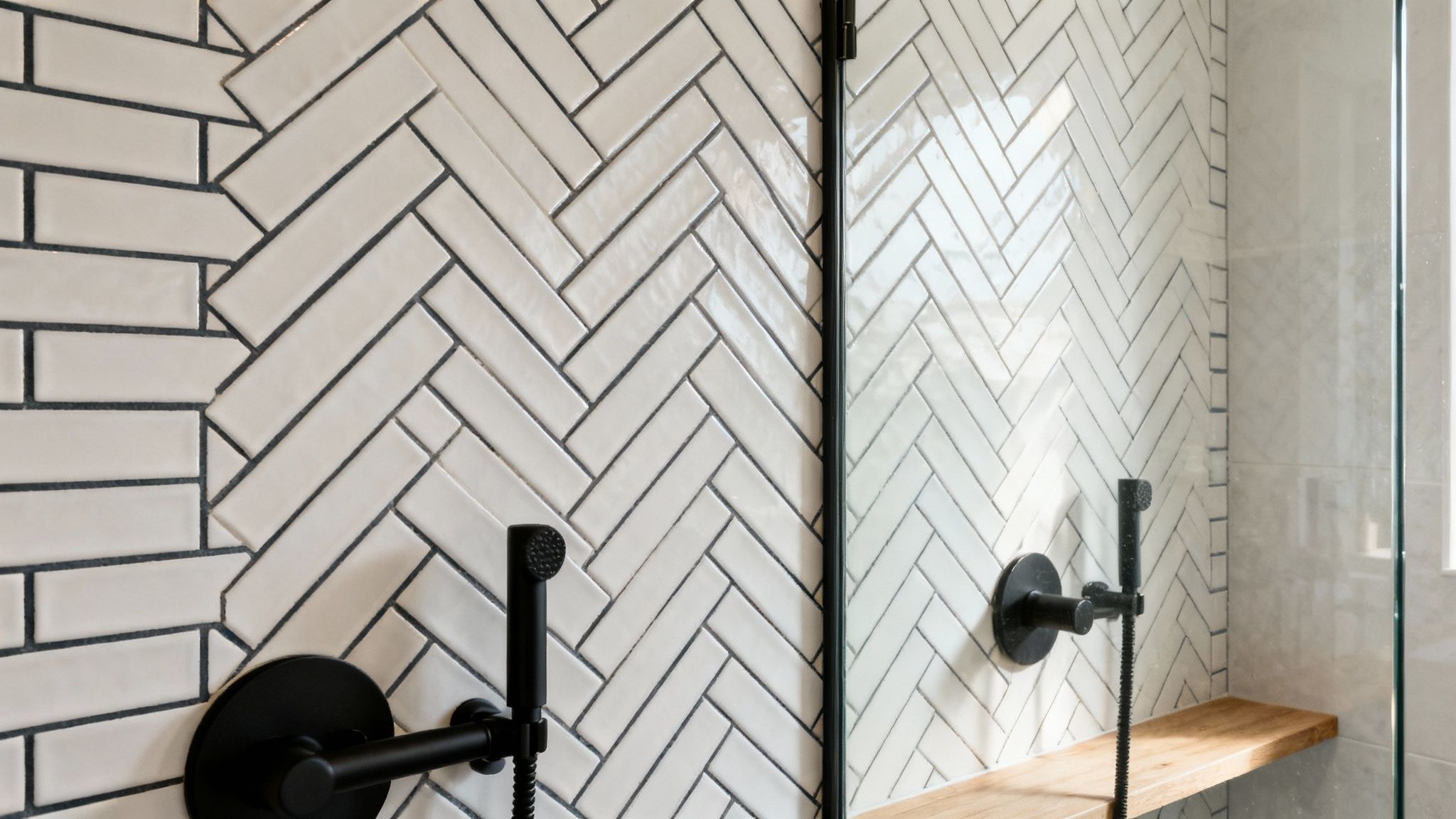 Modern bathroom shower with white herringbone tile pattern and black fixtures behind glass door