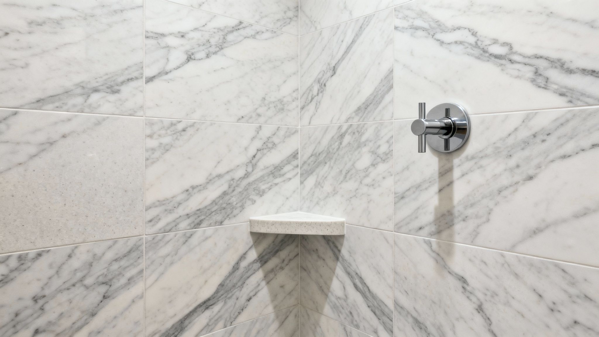 Modern shower corner featuring white marble tiles with gray veining and chrome fixtures with built-in shelf