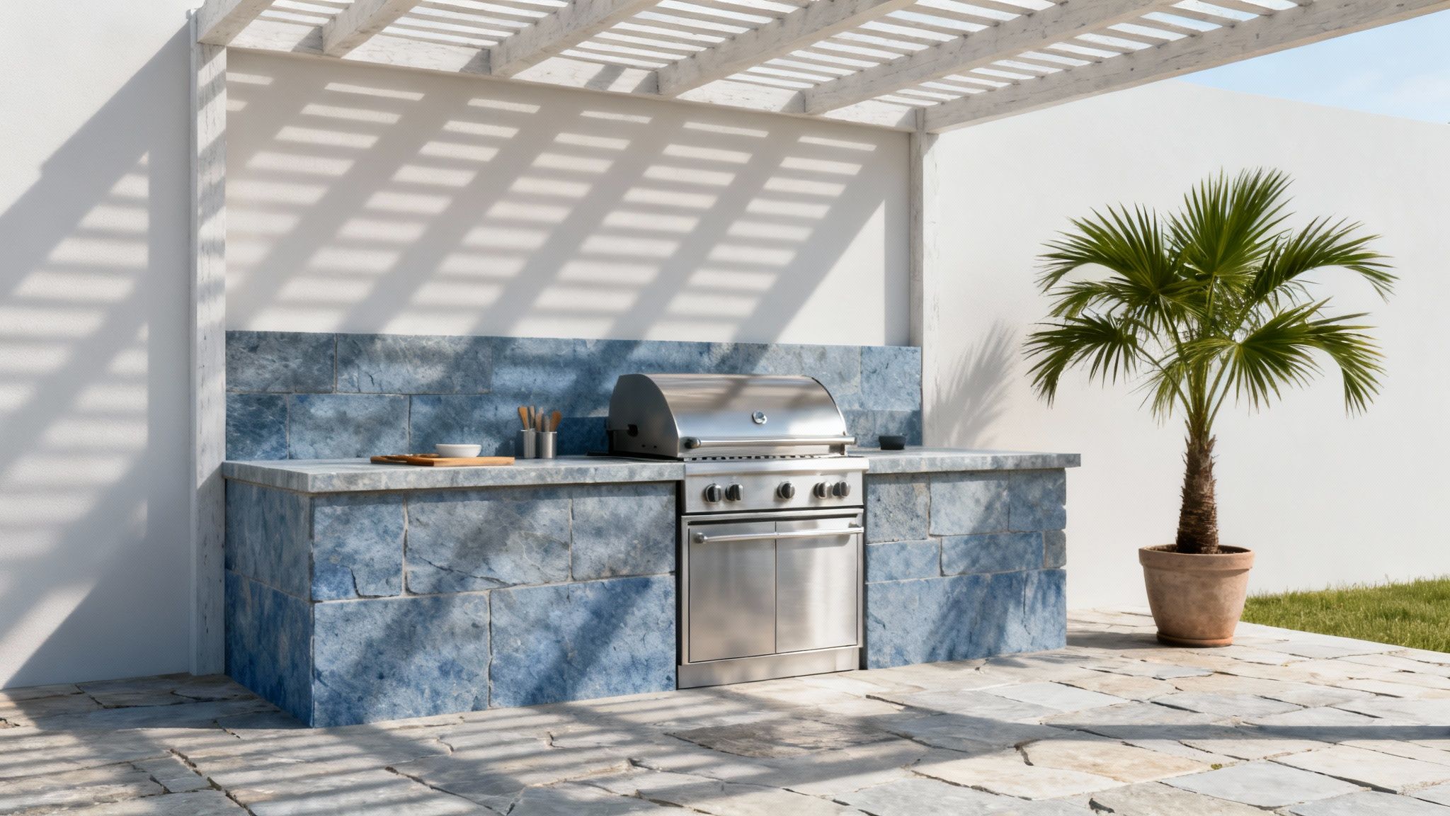 An outdoor kitchen with a built-in stainless steel grill, blue stone counters, and a potted palm tree.