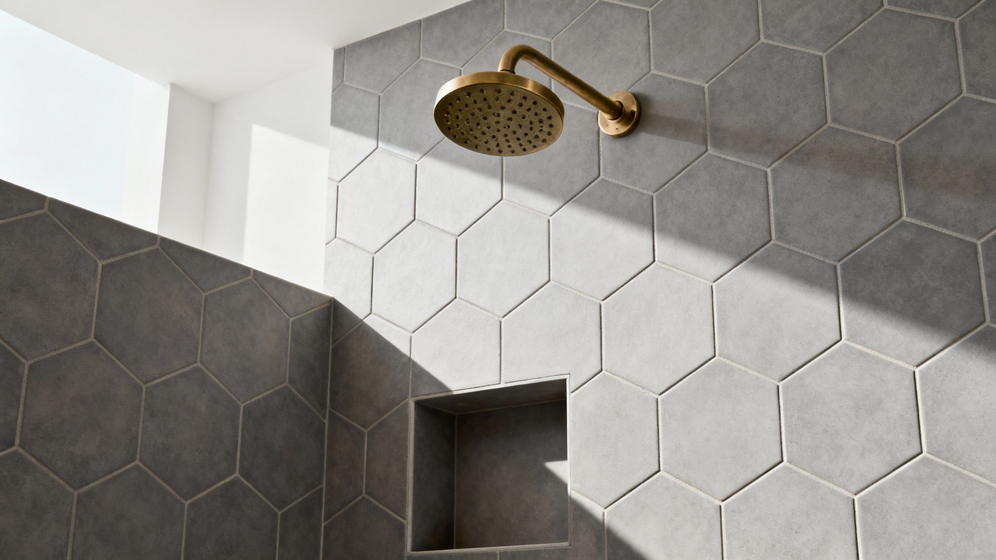 Modern bathroom featuring gray and white hexagon tiles with brass rainfall showerhead and built-in niche
