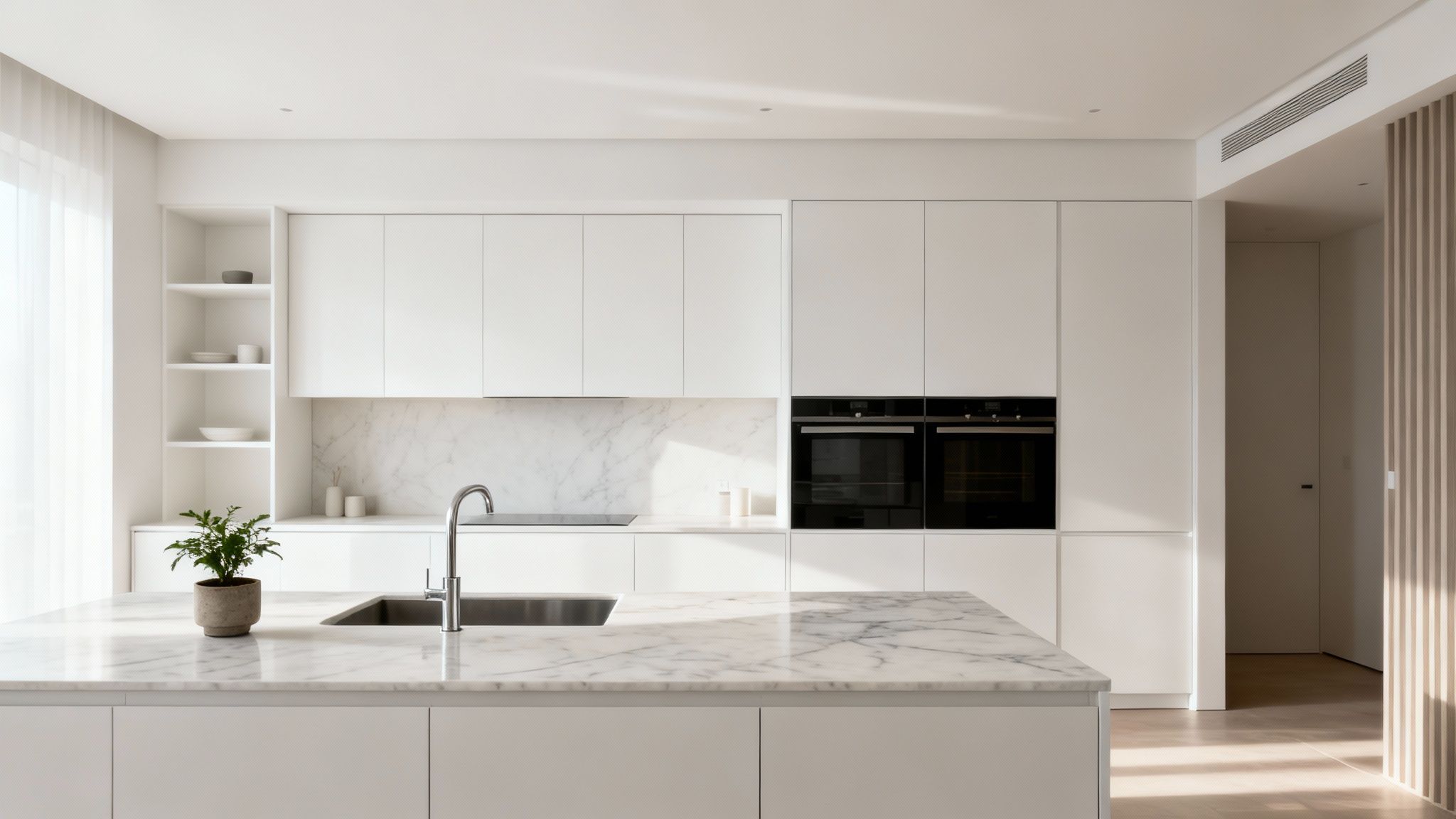 A sleek, modern white kitchen featuring marble countertops, an island with a sink, and integrated appliances.