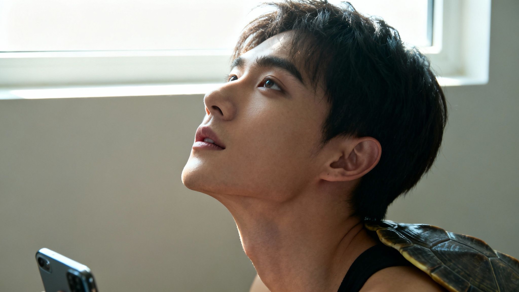 Profile of a young man looking up, with a turtle shell on his shoulder, holding a phone.