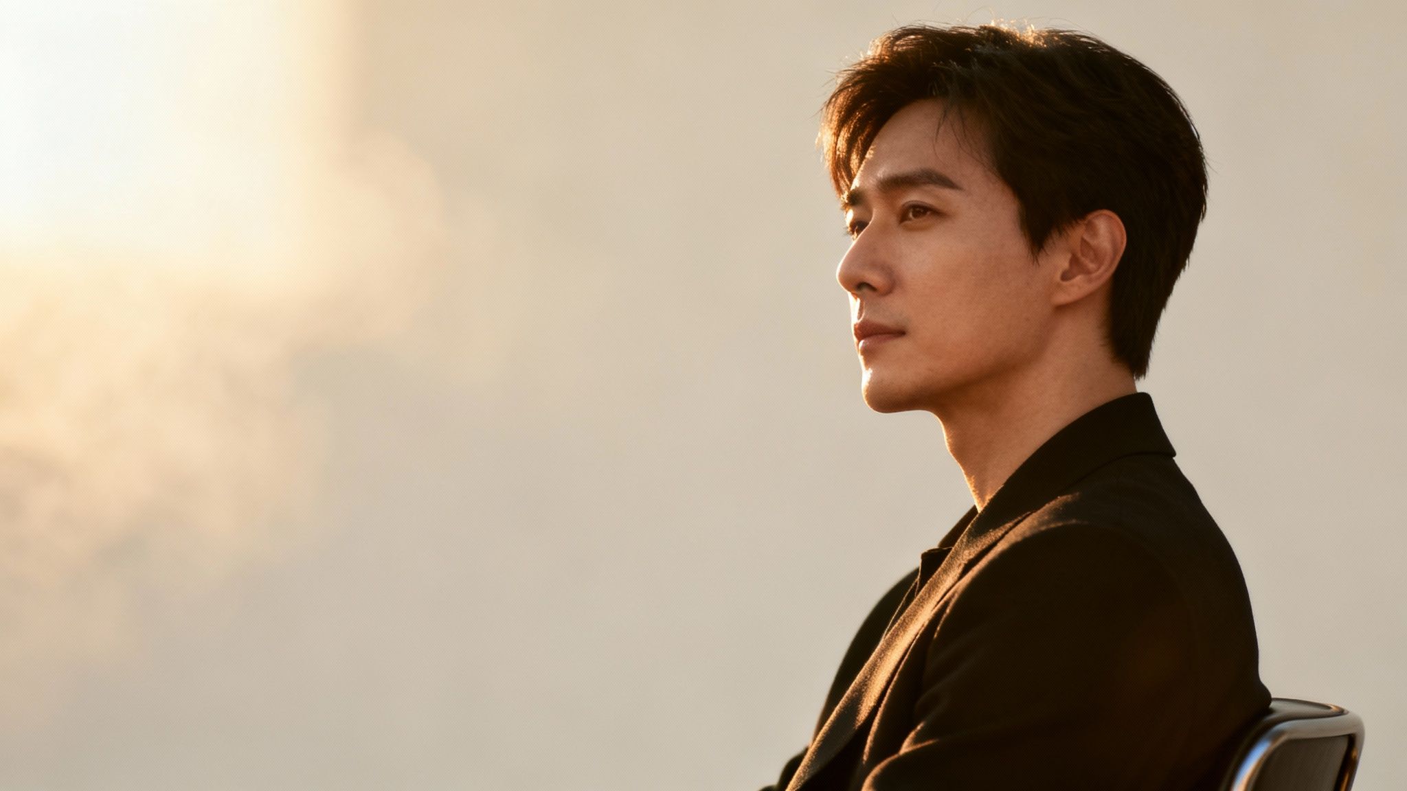 Profile of a thoughtful Asian man in a dark jacket, bathed in warm golden light.