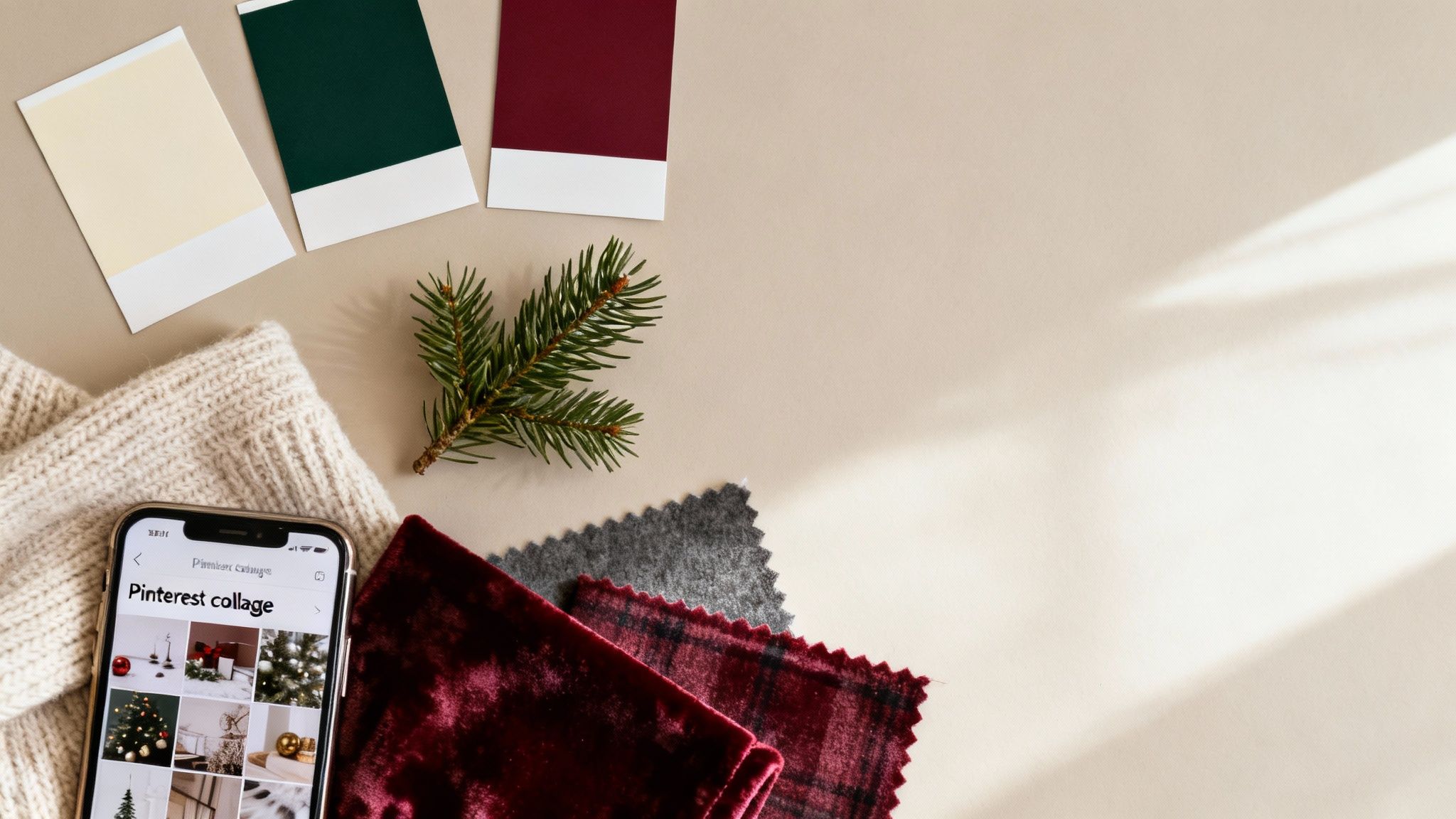 A flat lay of Christmas color swatches, a pine branch, knitted fabric, and a smartphone displaying a Pinterest collage.