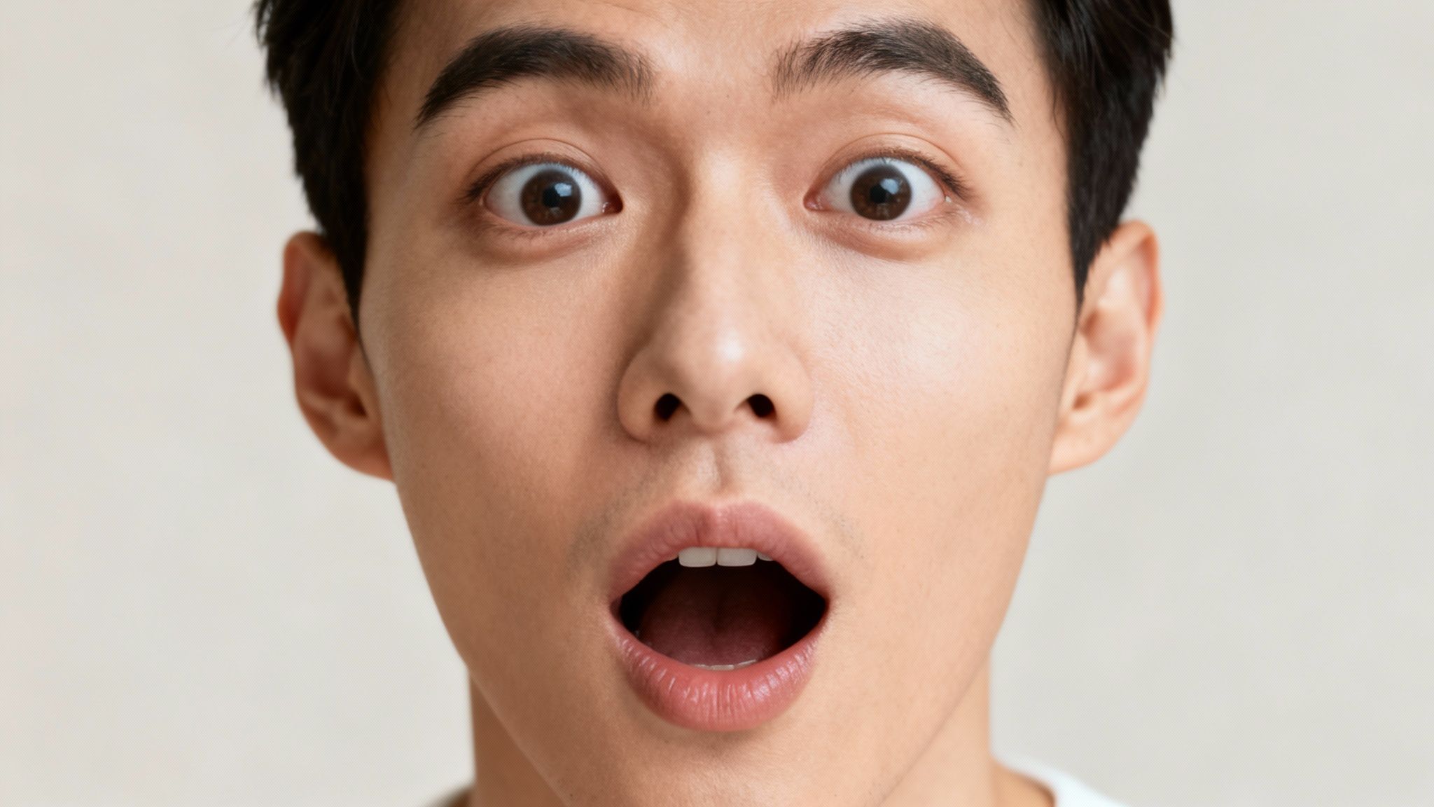 Close-up of a young Asian man with wide eyes and an open mouth, expressing shock or surprise.
