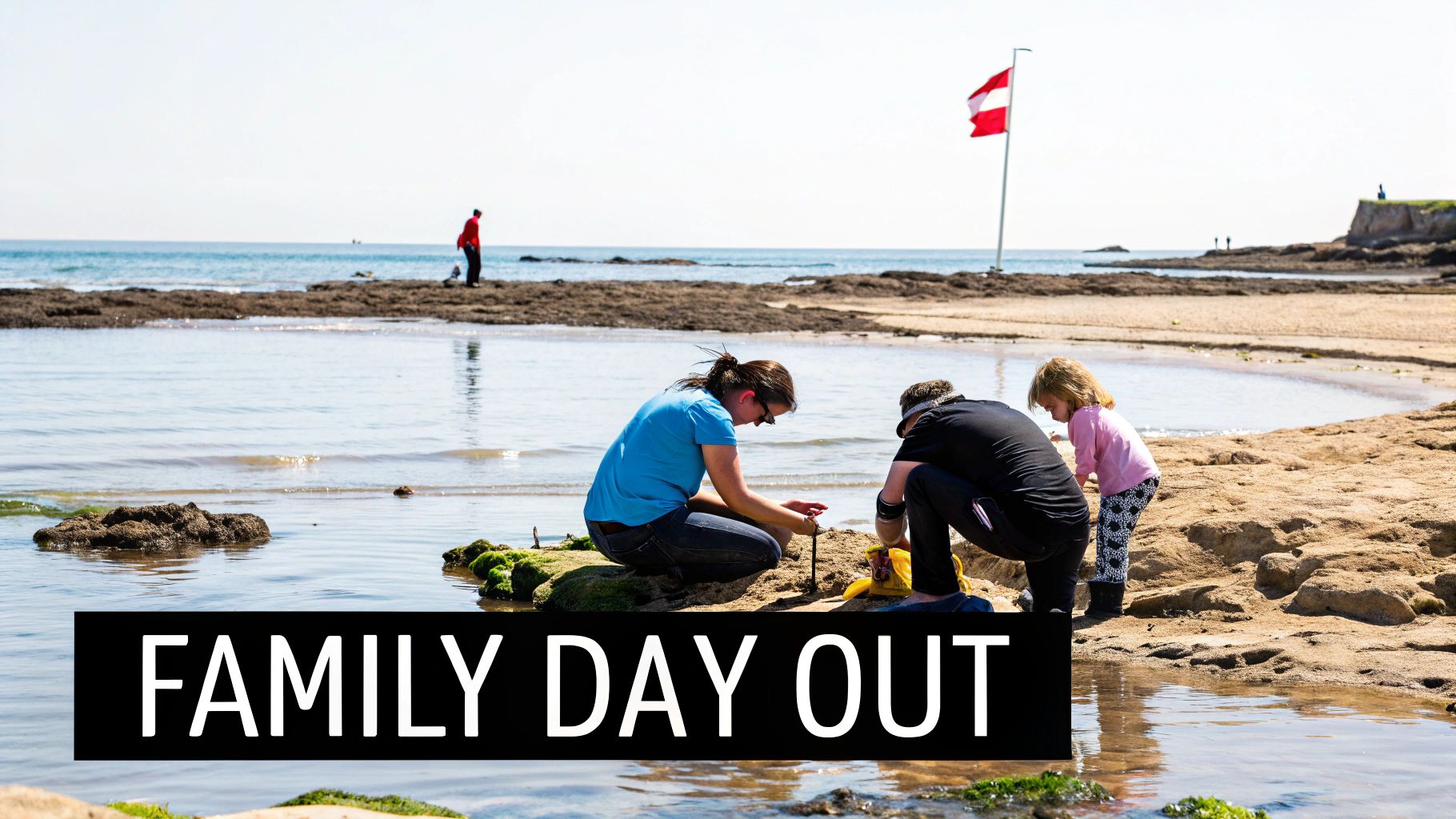A family, including two adults and a child, enjoys a sunny day playing on a sandy beach with water and rocks.