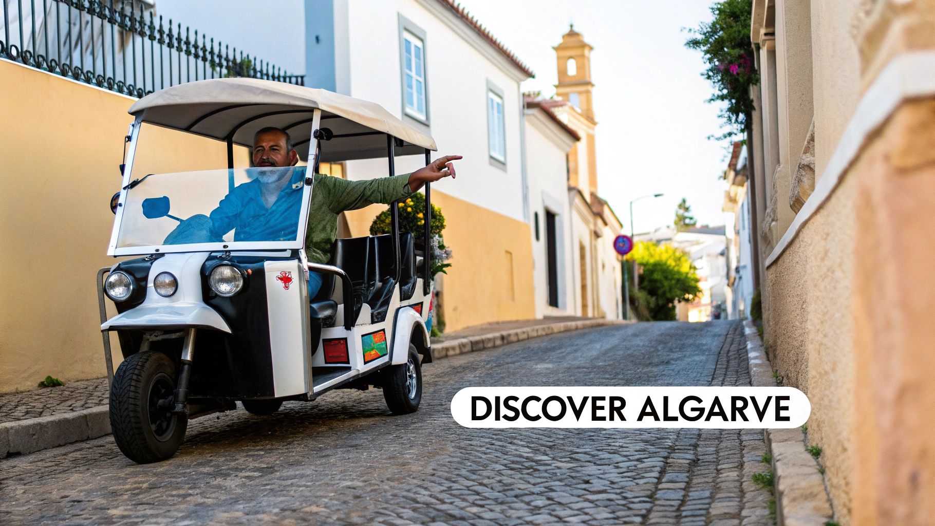 A man drives a white and black tuk-tuk on a cobbled street, pointing forward, with traditional buildings in the background.