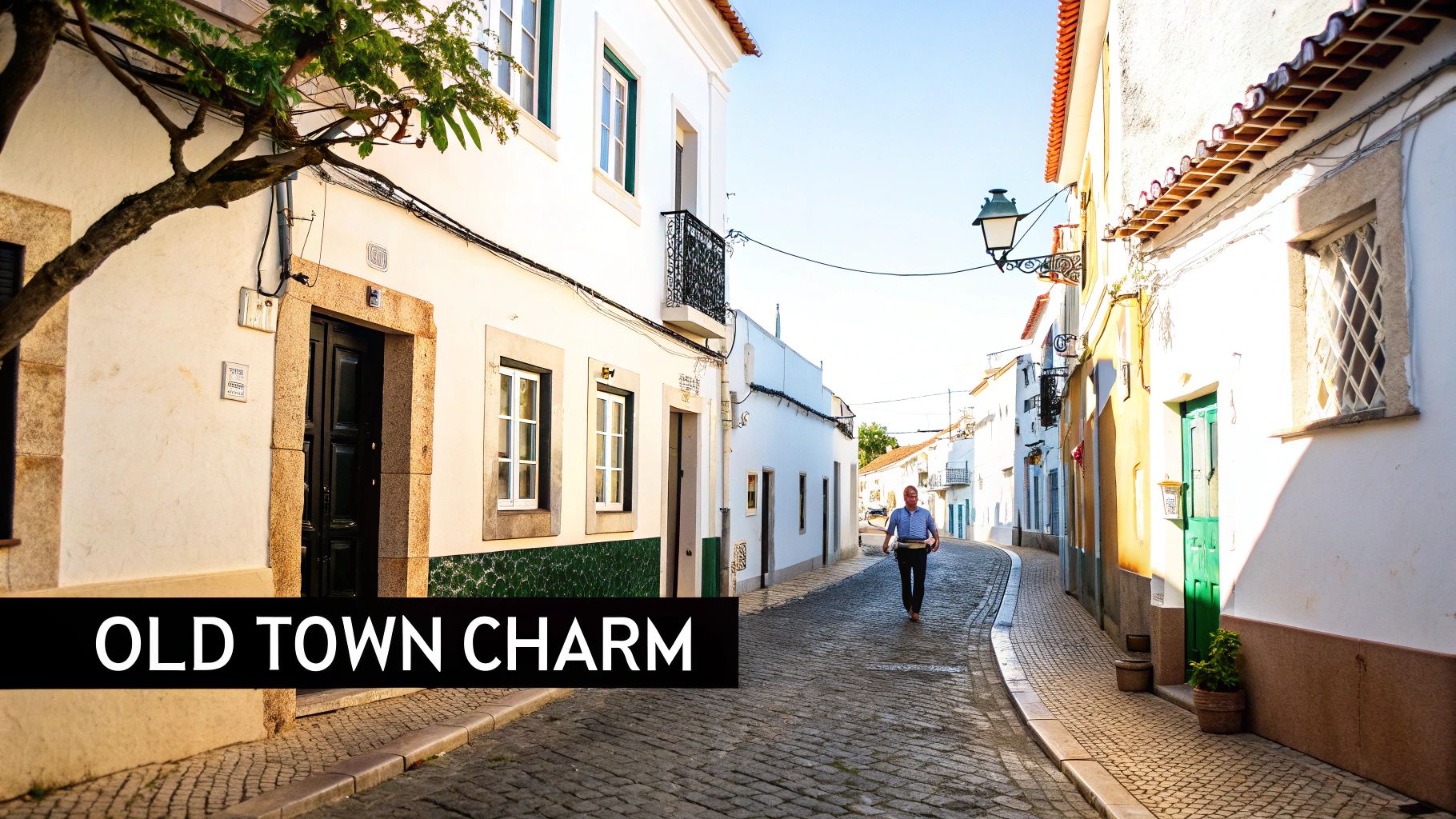 A charming cobblestone street in an old Portuguese town with white buildings and a person walking.