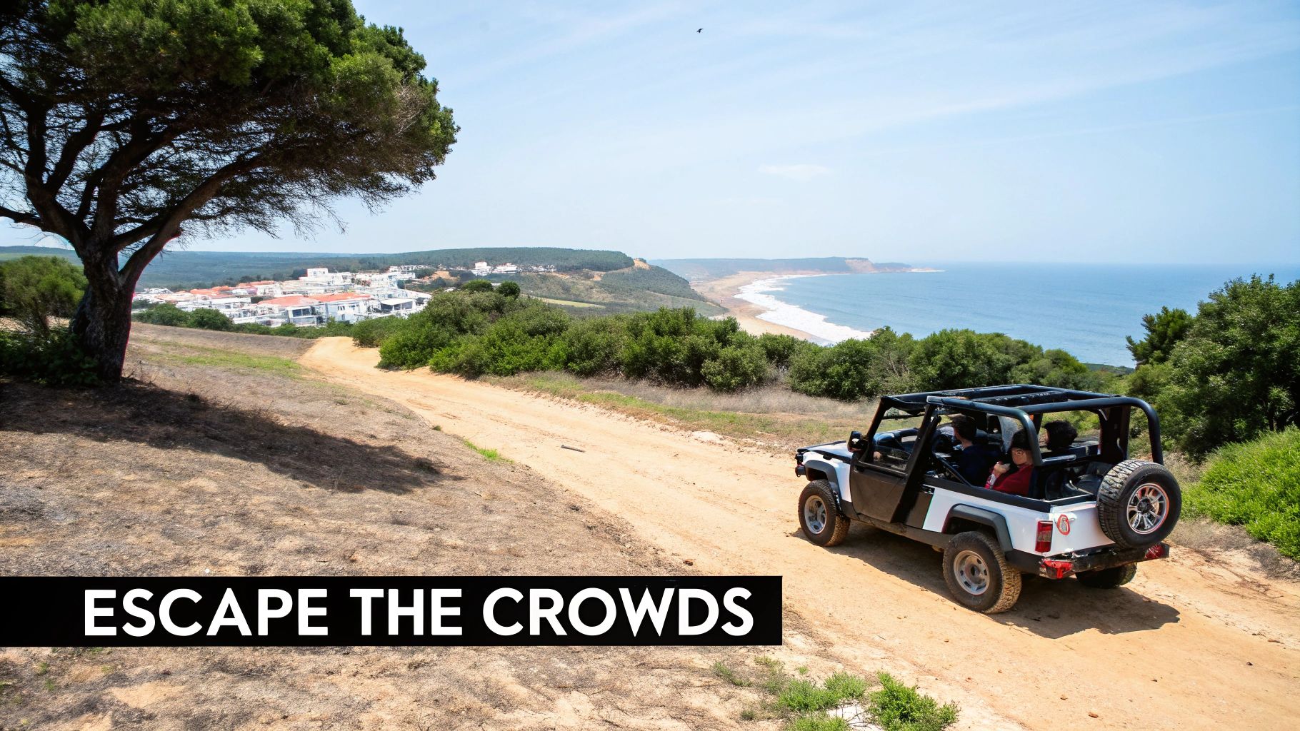 A white jeep drives along a dirt track, with a coastal village and ocean in the background.