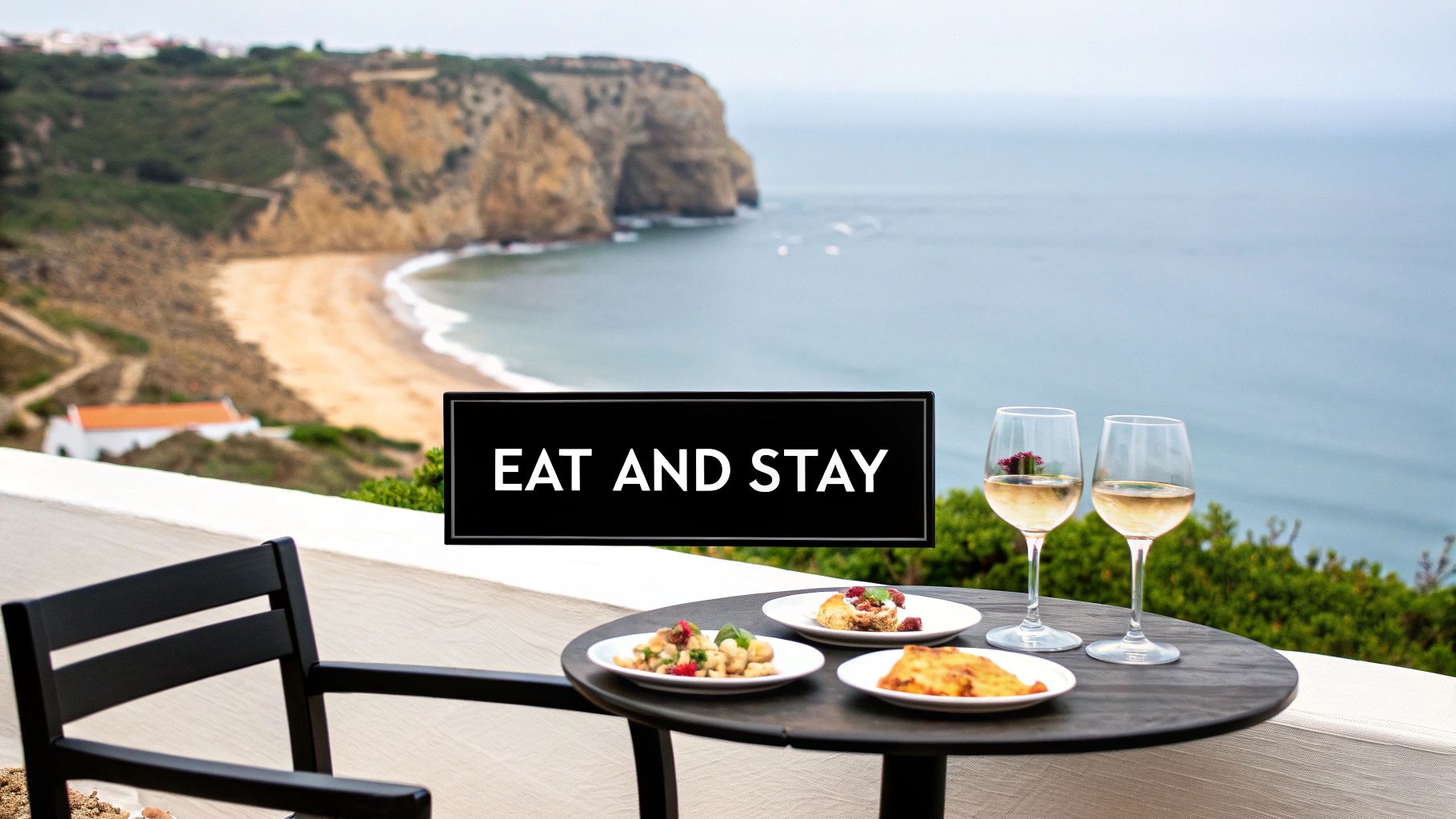 Outdoor dining table with food and wine, a sign 'EAT AND STAY', and stunning beach views.