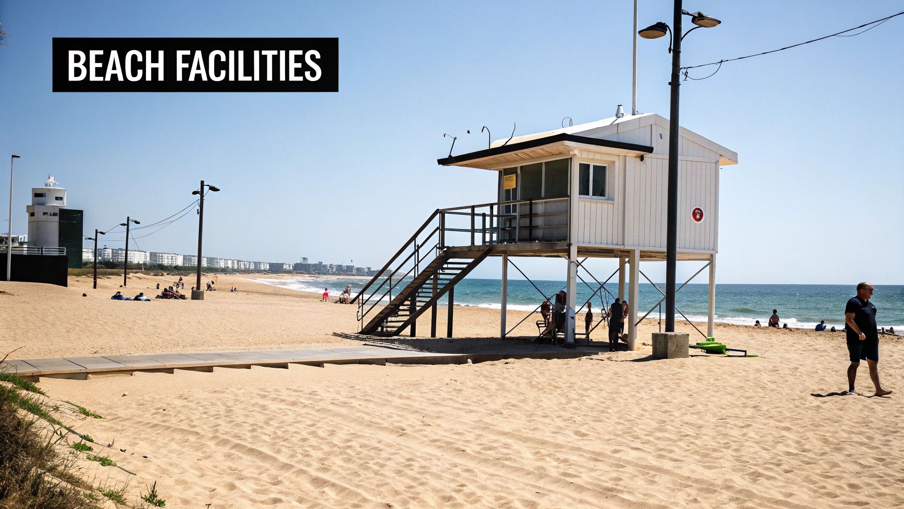 A sunny beach with a white lifeguard station on stilts, people relaxing, and the ocean.