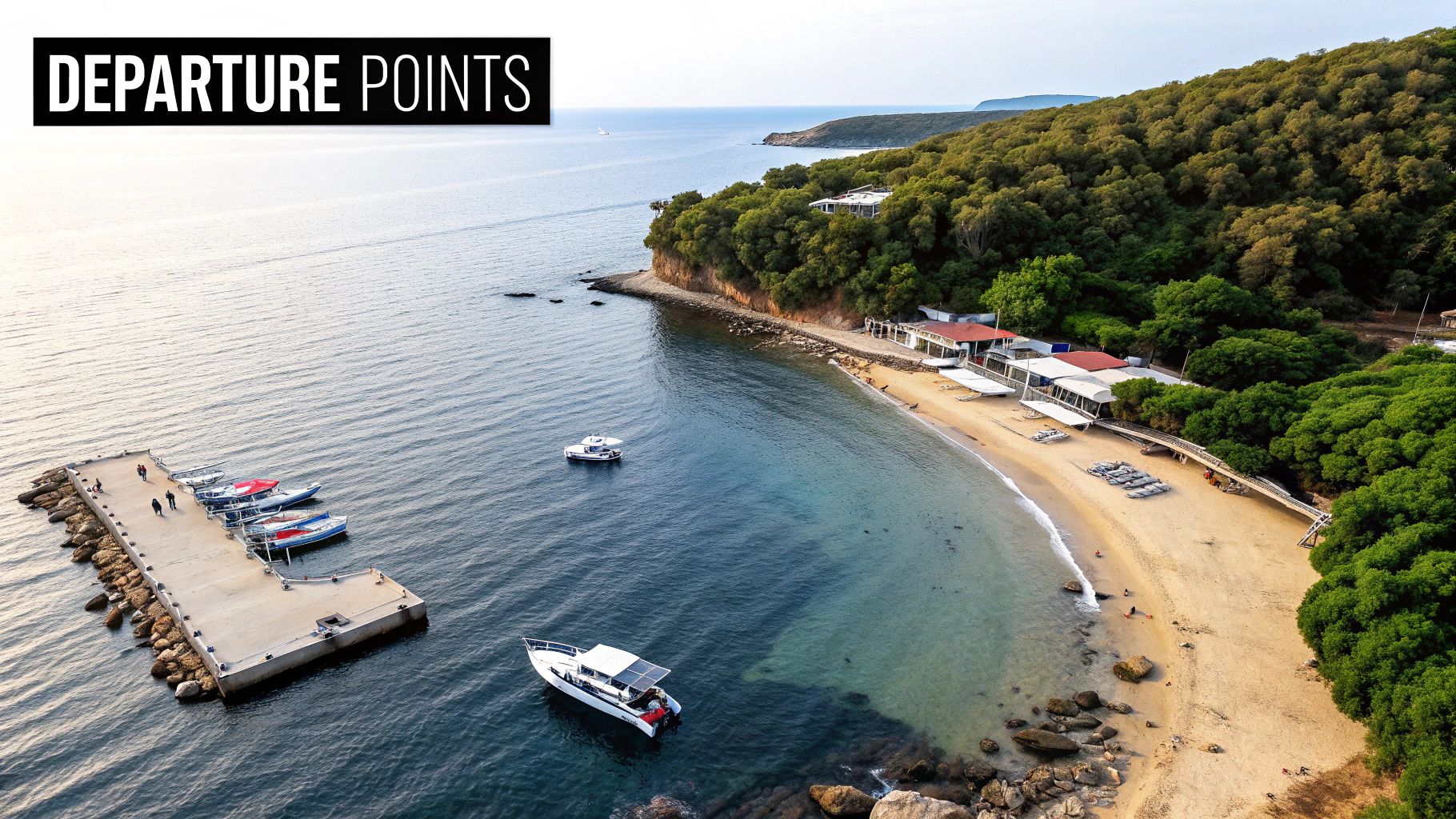 Aerial view of a picturesque coastal bay featuring a concrete pier with boats, a sandy beach, and green hills.