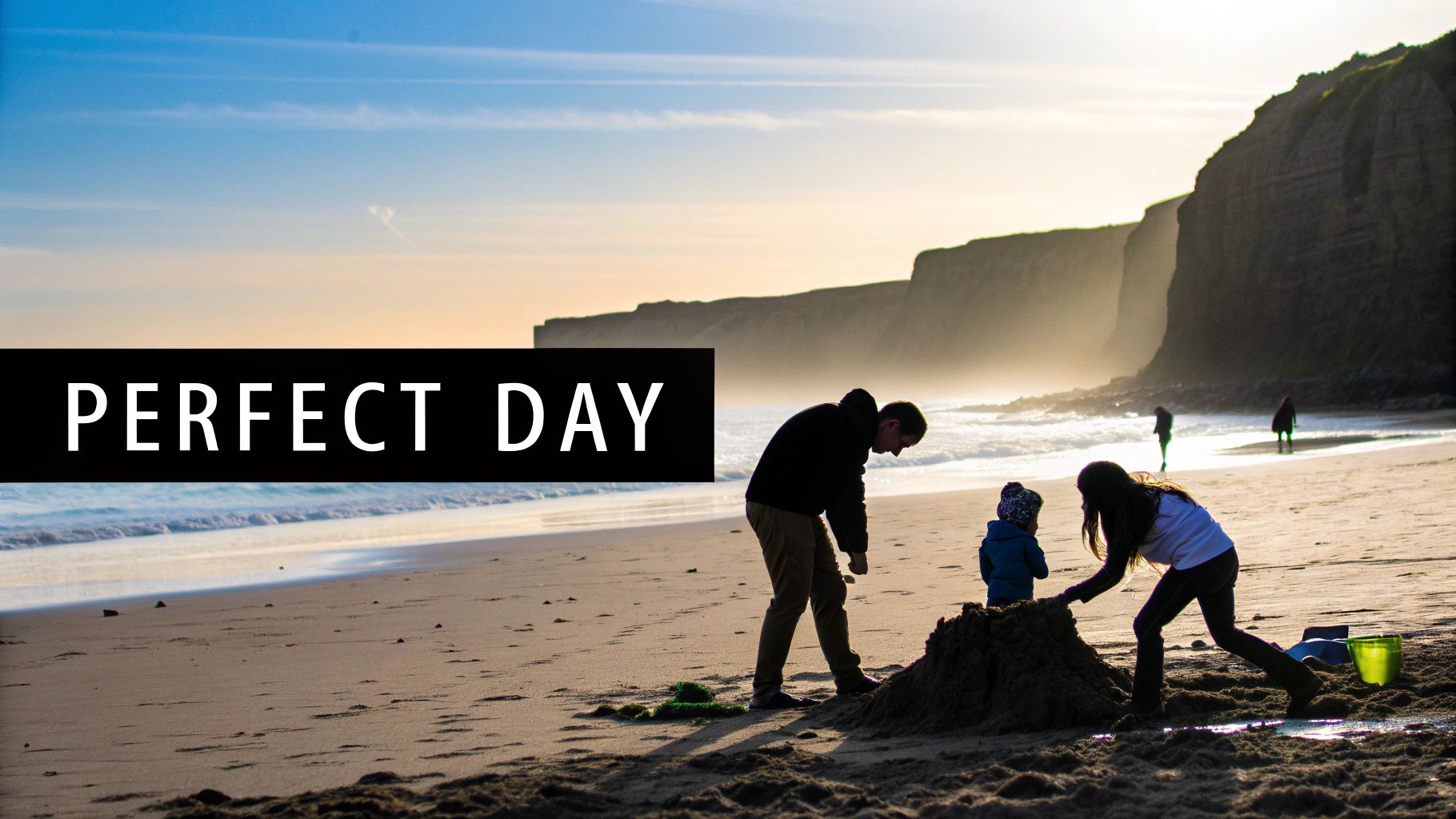 Family building a sandcastle on a sunny beach with cliffs and ocean waves, featuring text 'PERFECT DAY'.