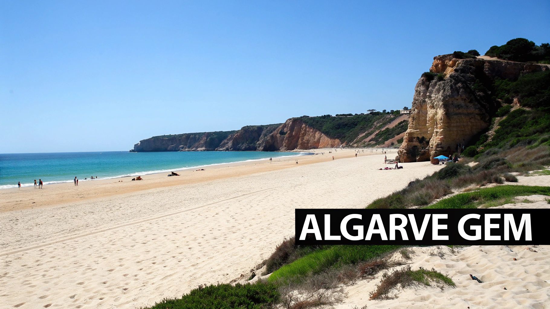 A sunny wide sandy beach with clear blue ocean, rugged cliffs, and people enjoying the water.