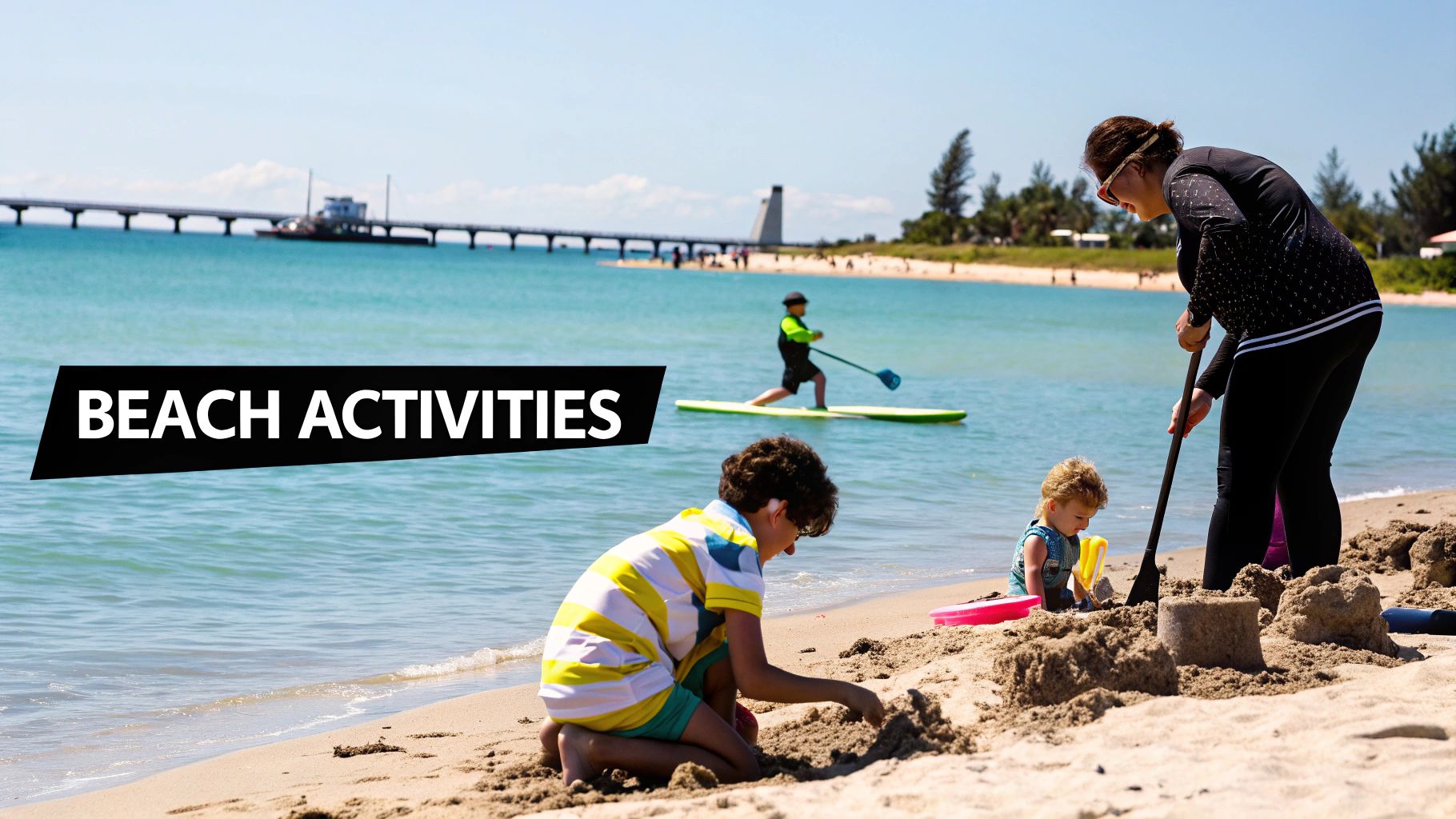 A family enjoys beach activities, with kids building sandcastles and a child paddleboarding near a pier.