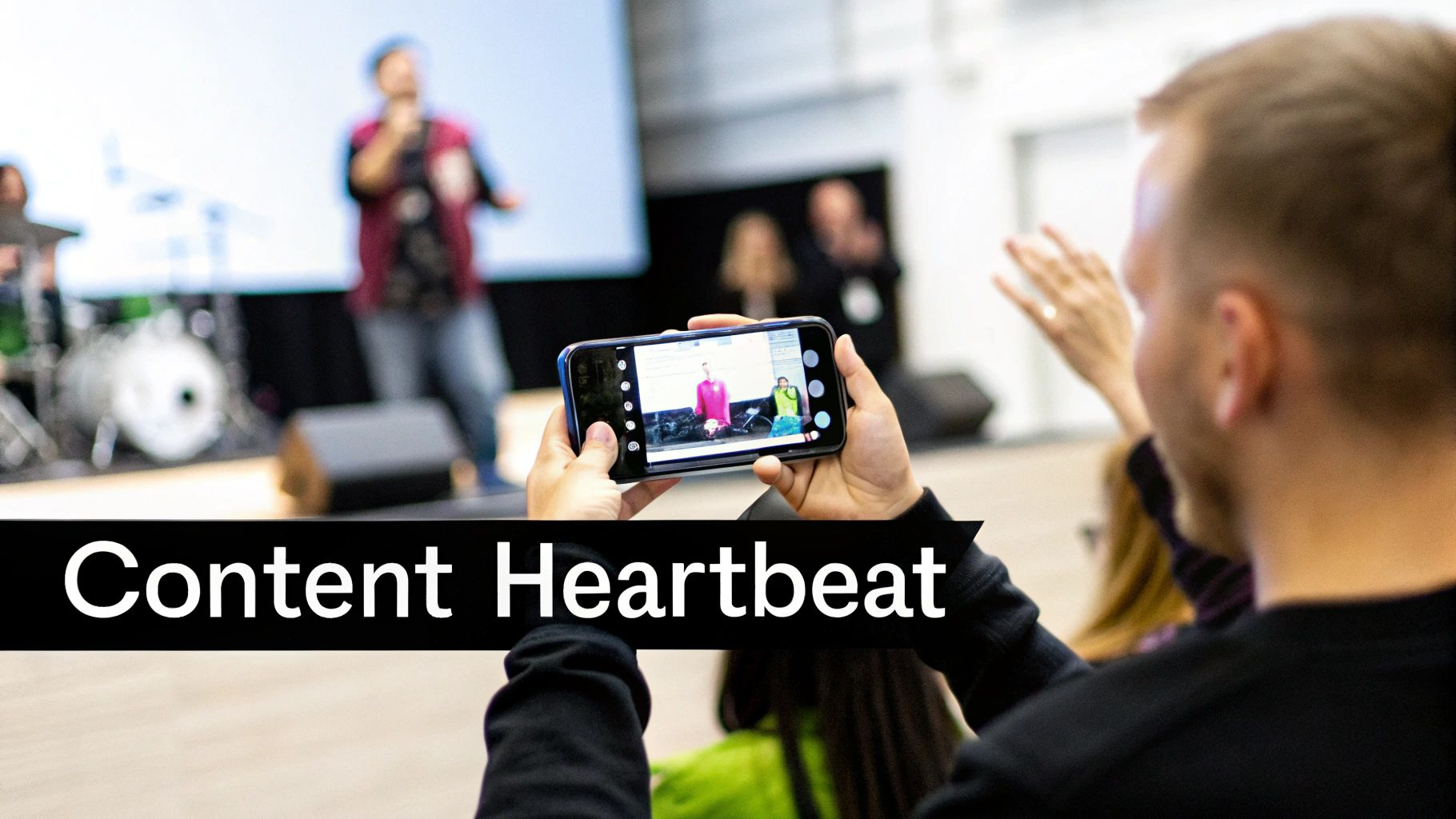 Person recording a stage speaker with a smartphone at an event, creating live content.