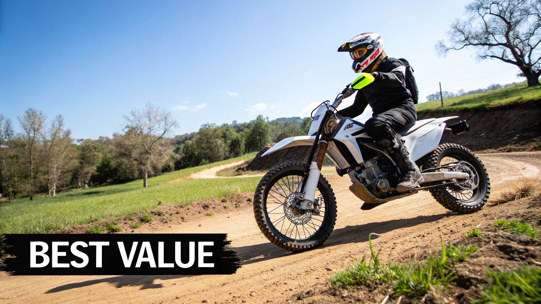 A rider on a white electric dirt bike navigates a dusty trail through green hills under a blue sky.