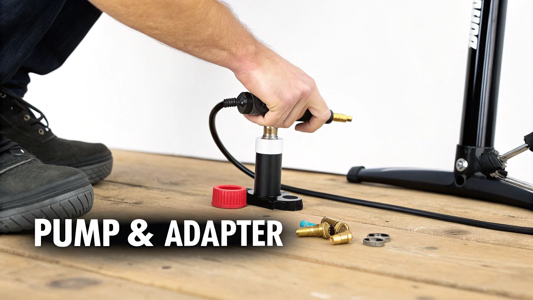 A person's hands using a small pump, with various valve adapters on a wooden floor.