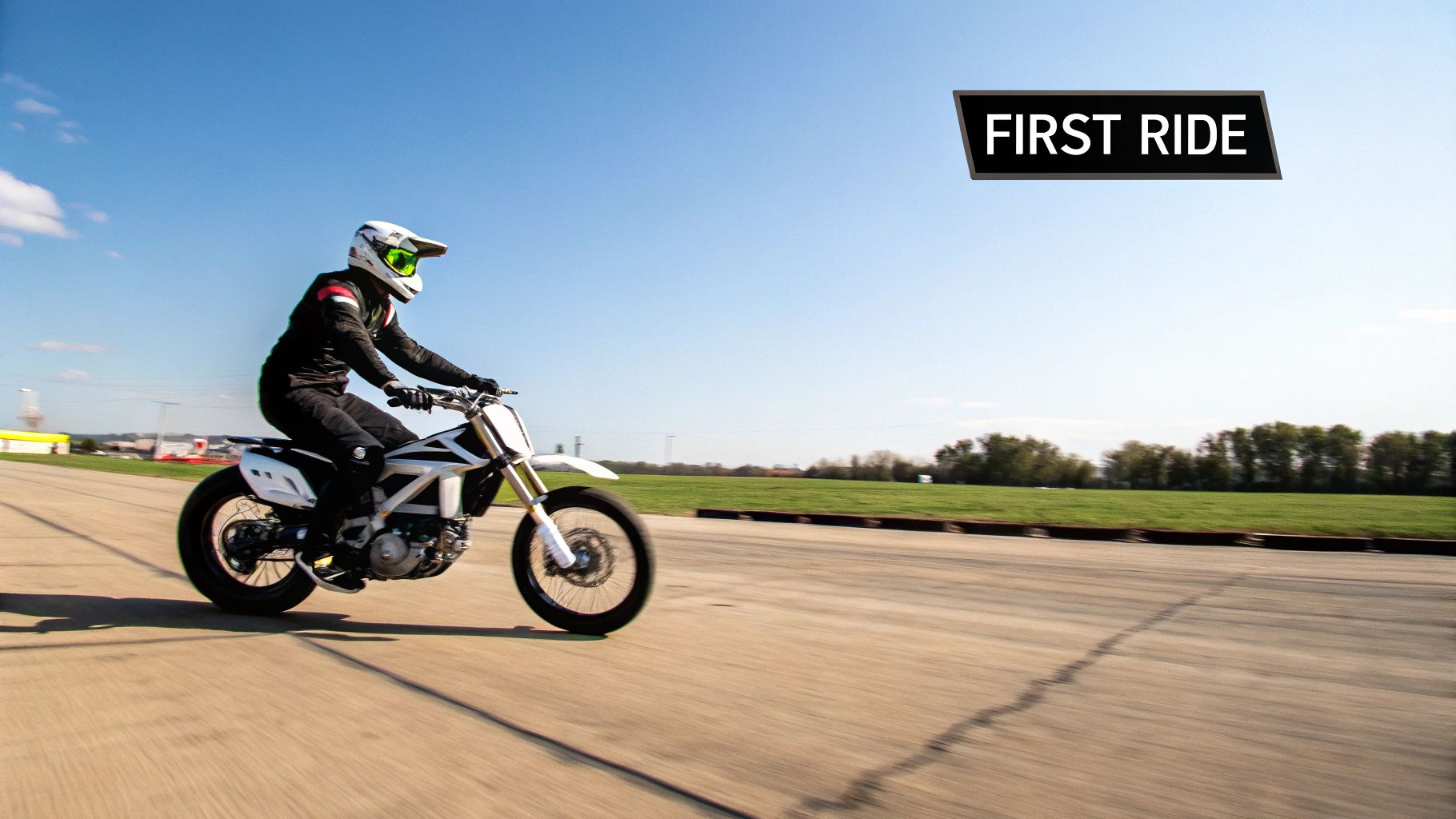 A person in full gear riding a white dirt bike on an open asphalt track under a blue sky.