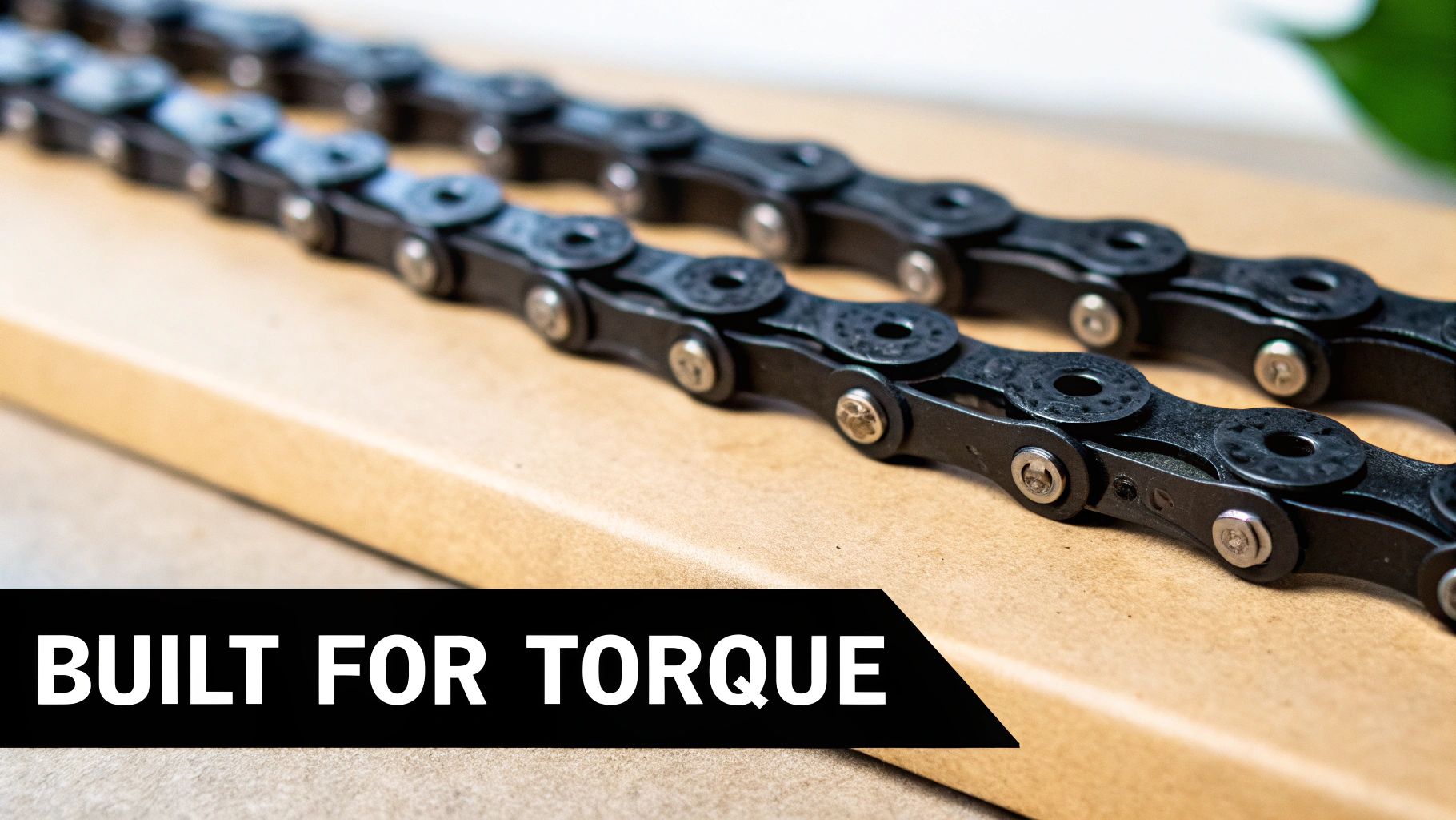 Close-up of two parallel heavy-duty black bicycle chains with silver rivets resting on a wooden surface, featuring text 'BUILT FOR TORQUE'.