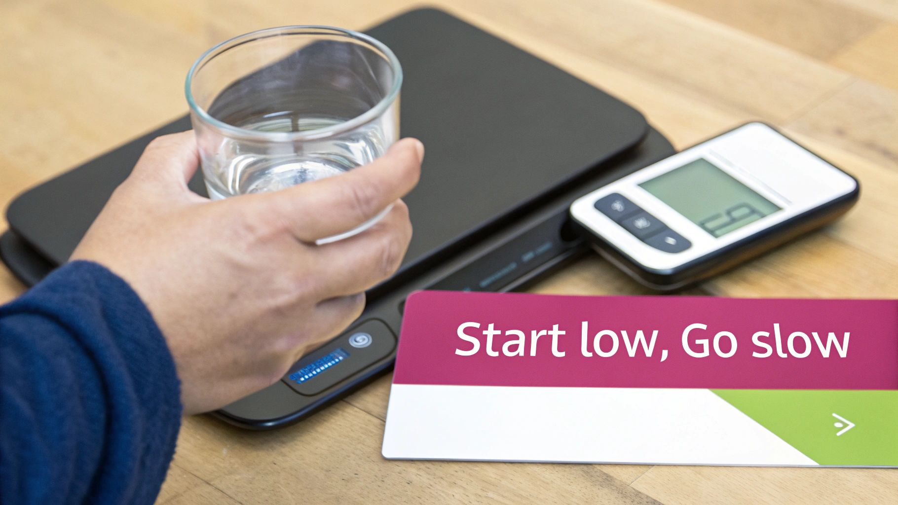 A person's hand holds a glass of water above a digital kitchen scale, with a "Start low, Go slow" card nearby.