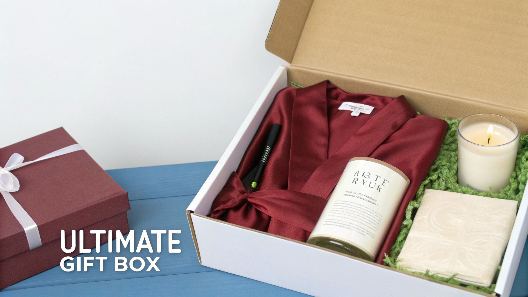 An open white gift box reveals a red satin robe, a black pen, a candle, and a folded item on green filler, next to a closed red gift box.
