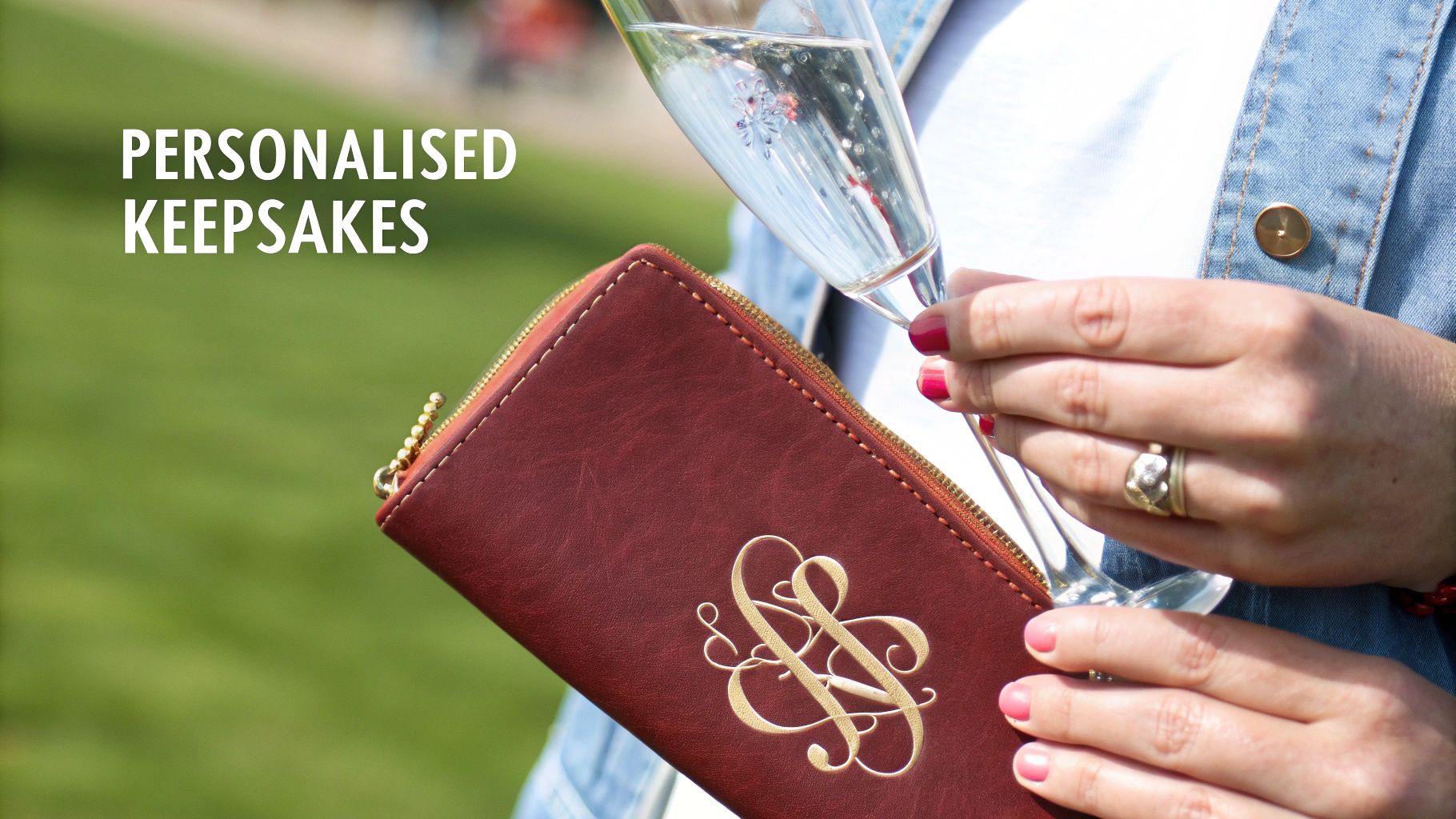 A person holds a champagne flute and a personalized deep red wallet with gold monogram, hinting at a celebration.