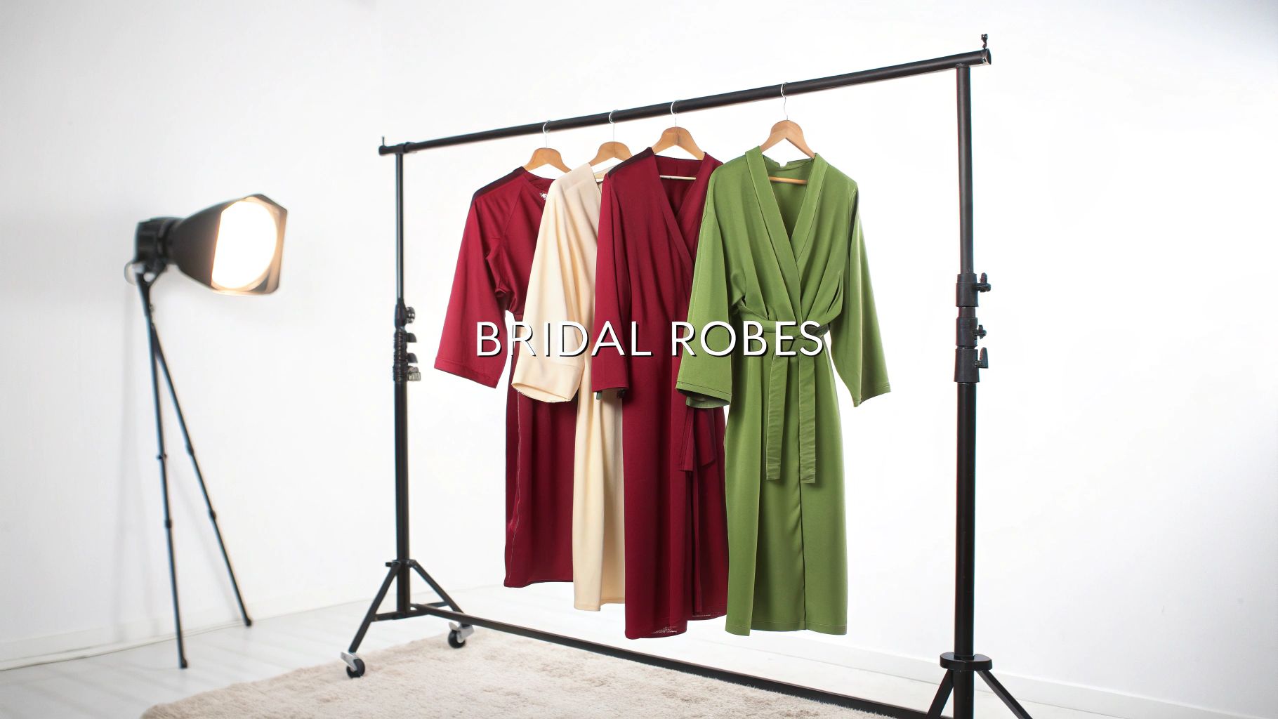Four bridal robes in maroon, cream, and olive green hanging on a rack in a studio.