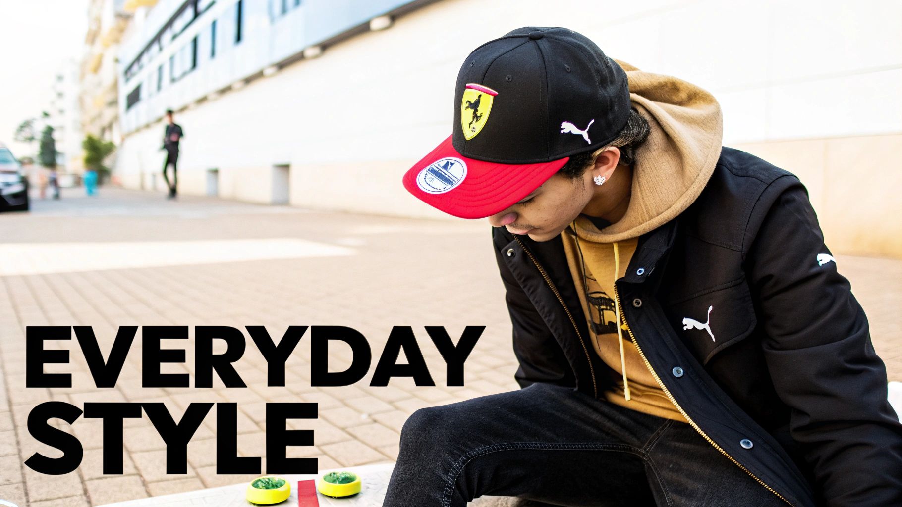 Stylish young person wearing a black Ferrari Puma baseball cap, black jacket, and yellow hoodie outdoors.