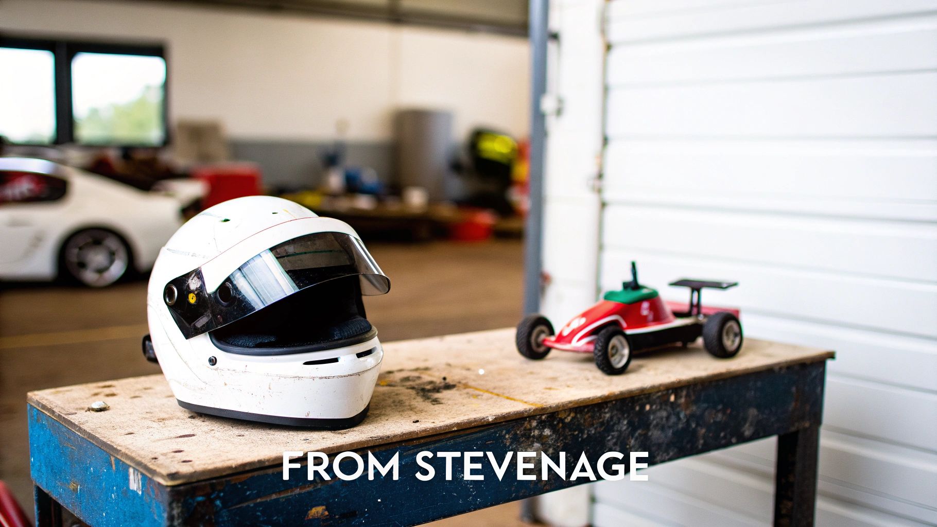 A white racing helmet and a red toy race car on a workbench in a garage setting.