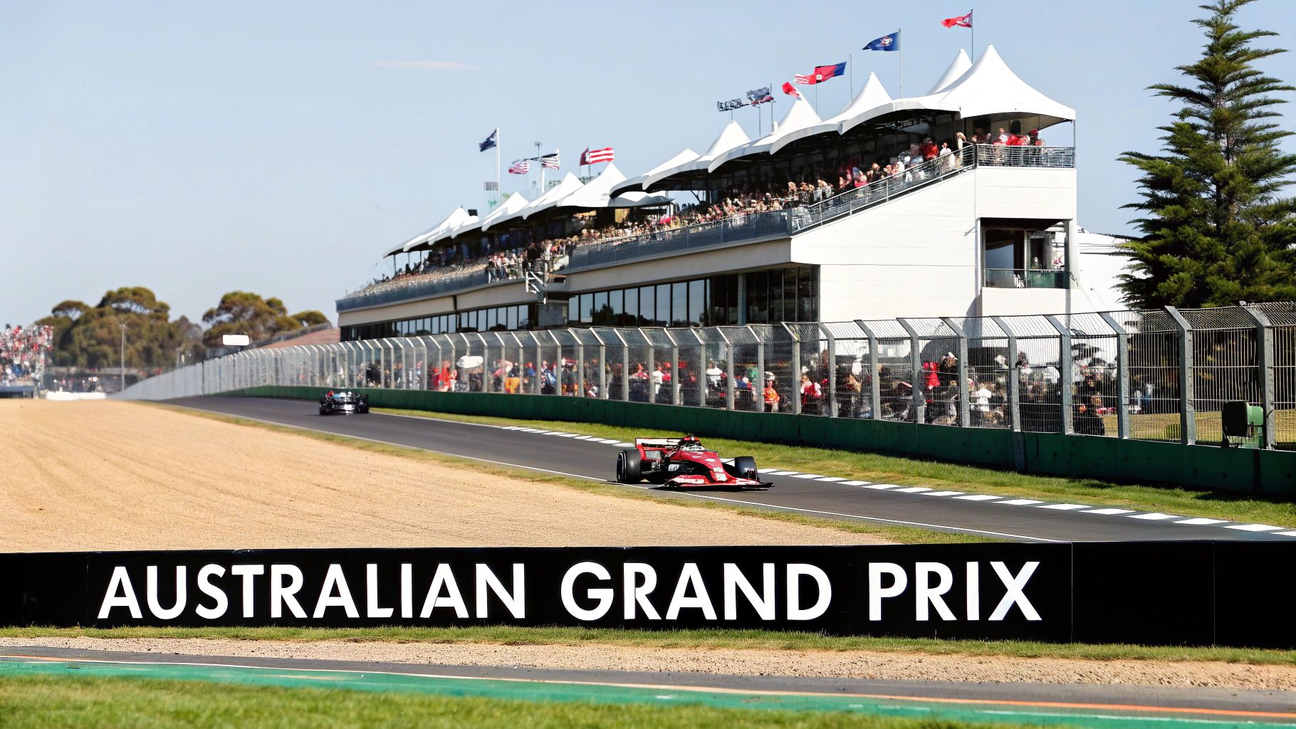 A red Formula 1 car races on the track past a crowded grandstand during the Australian Grand Prix.