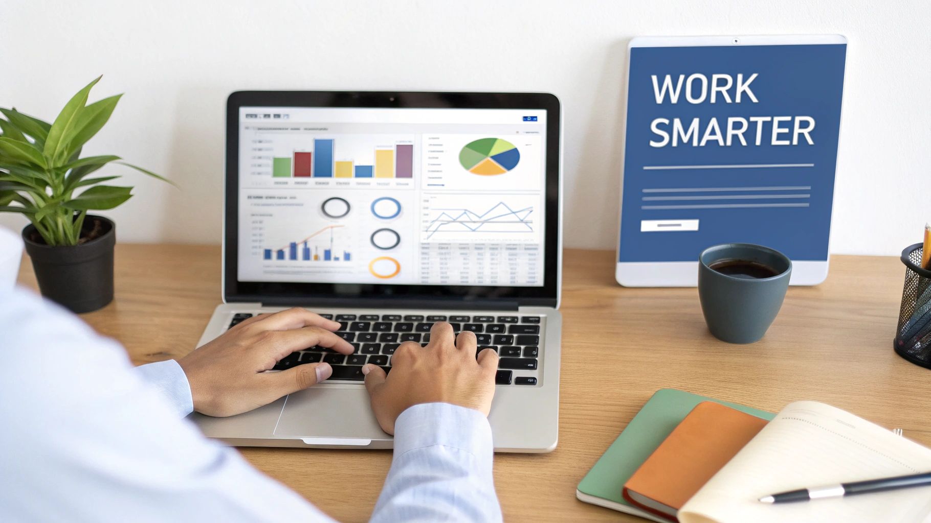 Person working on a laptop with data visualizations, a tablet displaying 'WORK SMARTER', and office essentials.