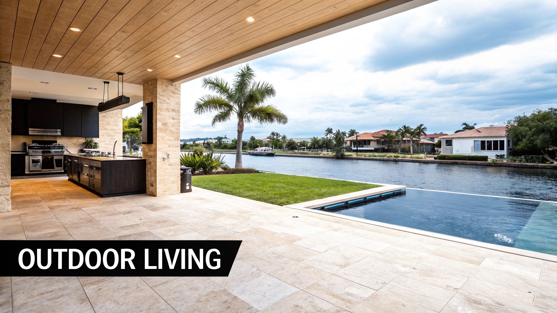Modern outdoor kitchen and infinity pool overlooking a scenic canal with waterfront homes.