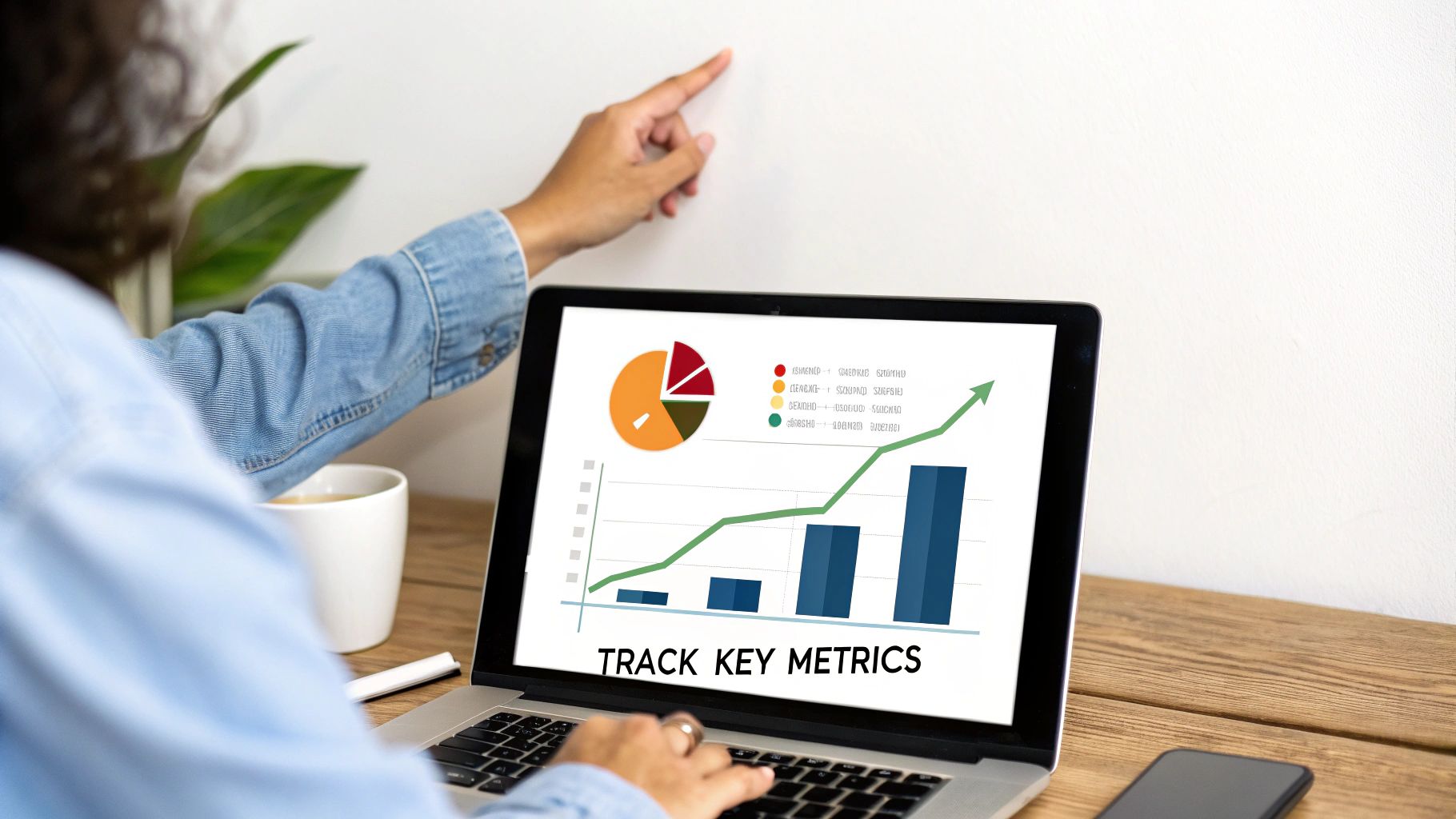 A person points at a laptop screen displaying business graphs, charts, and 'TRACK KEY METRICS'.