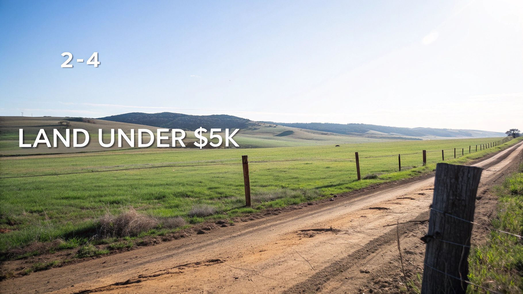 A dirt road runs alongside a wire fence and green fields with rolling hills under a clear blue sky.