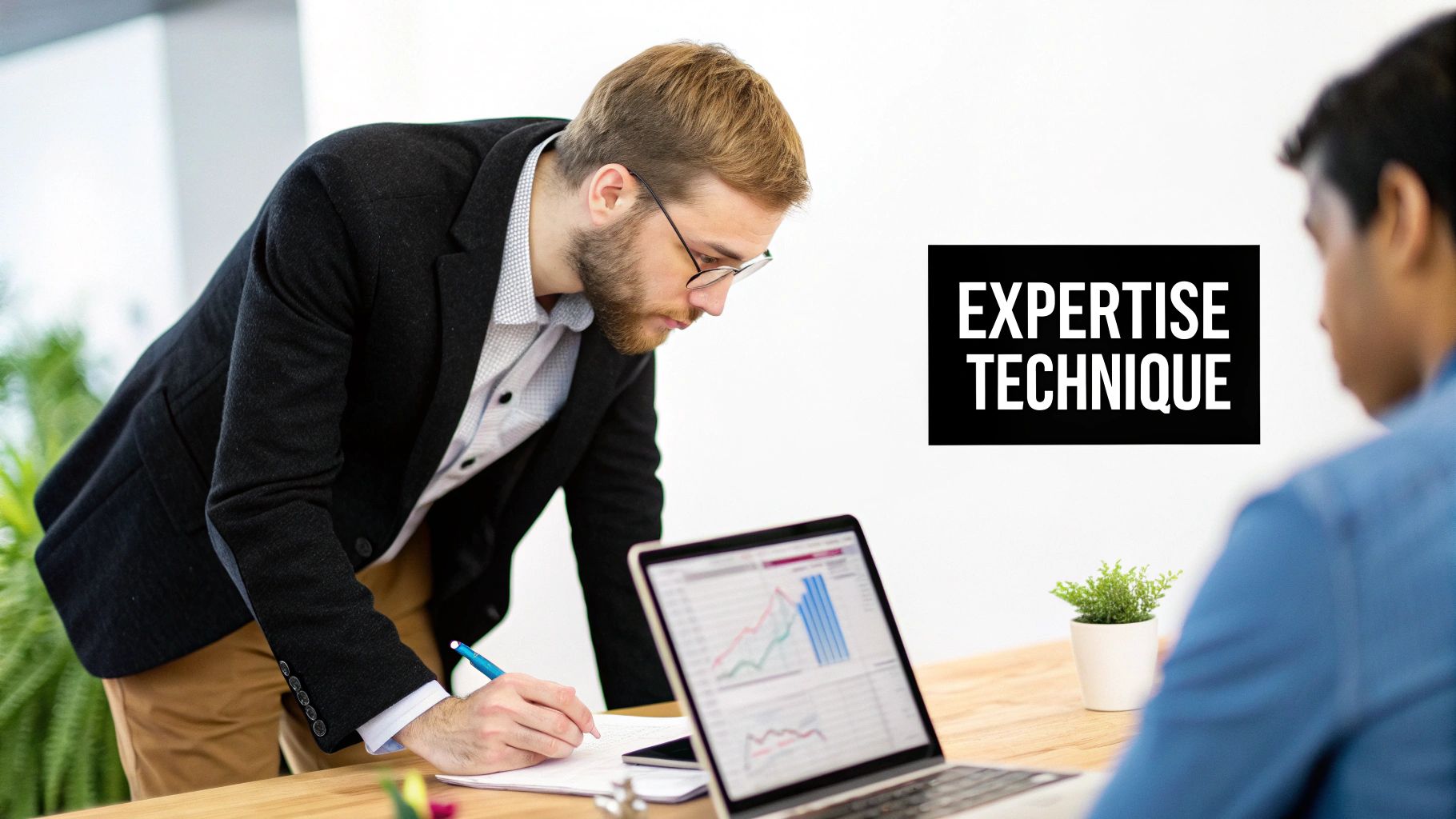 Deux hommes travaillent dans un bureau moderne. L'un écrit des notes, l'autre regarde un écran d'ordinateur portable affichant des graphiques.